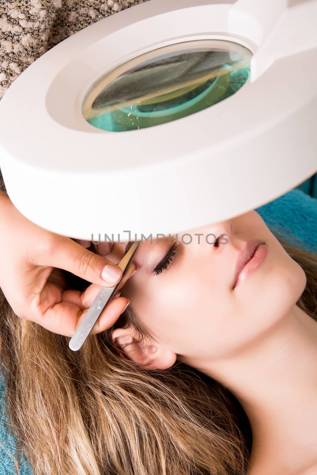 Woman getting tweezing eyebrow by beautician