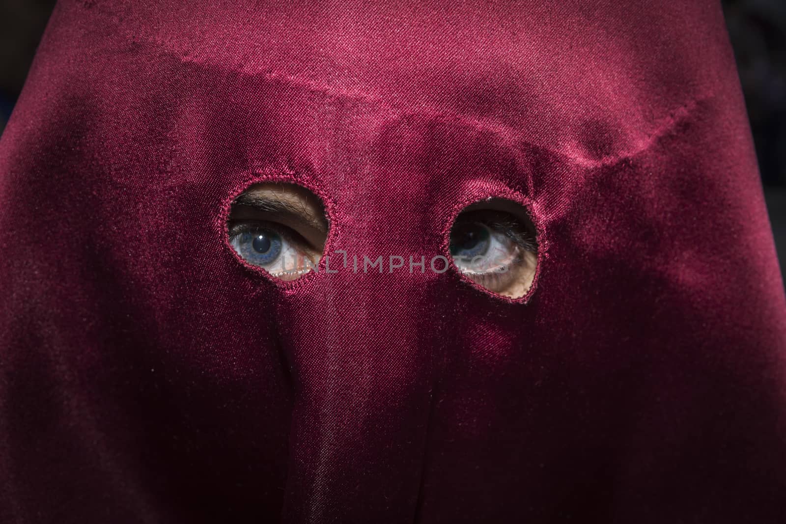 Detail of blue eyes of penitent with caperuz red during Holy Week in Spain