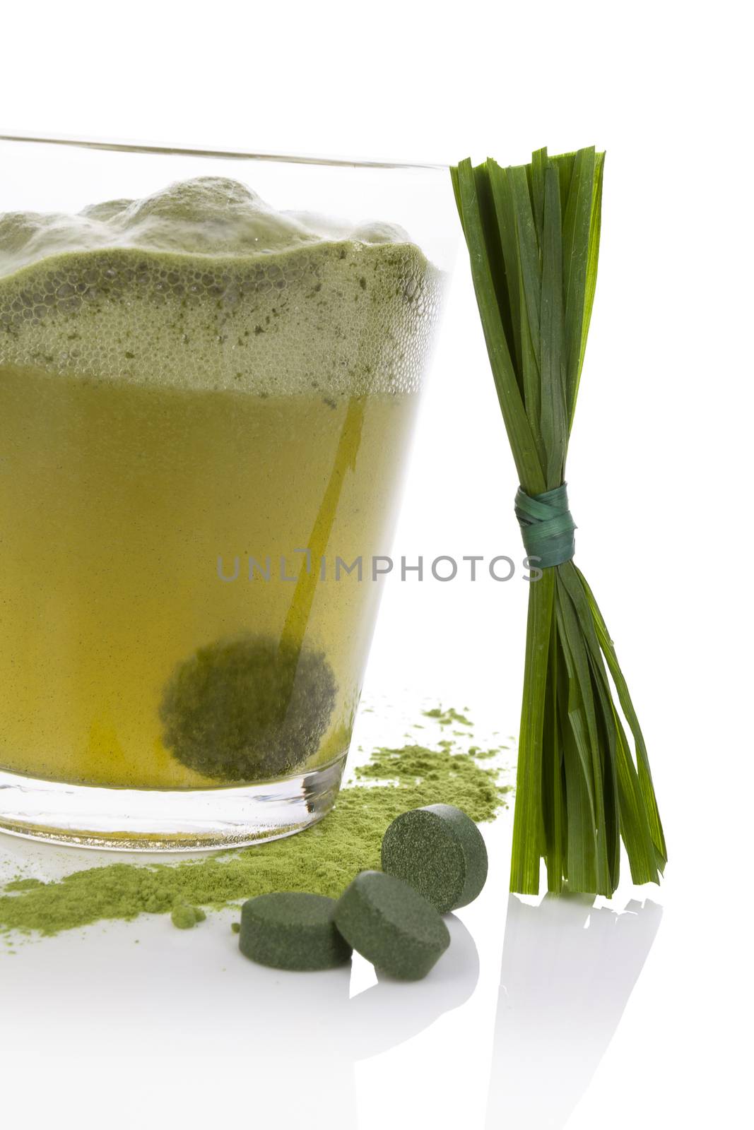 Green effervescent tablet dissolving in water. Green pills, green powder and grass blades isolated on white background. Natural detox. Healthy algae.