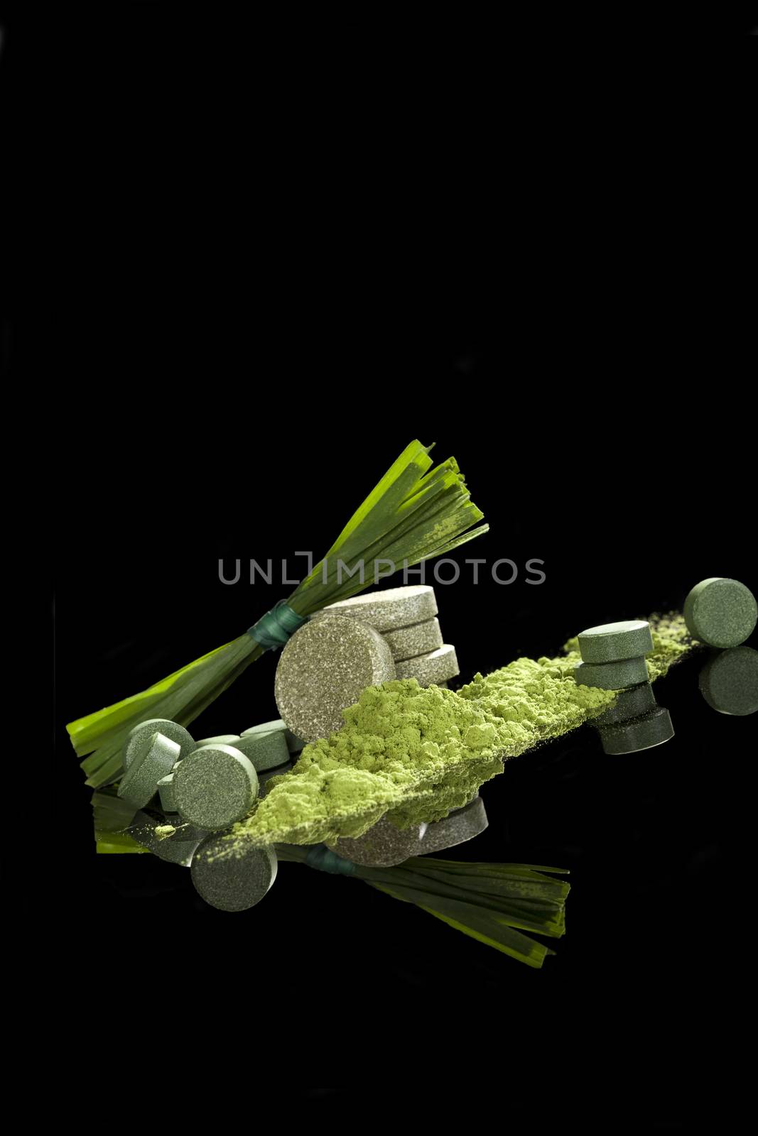 Green dietary supplements. Pills, ground powder, effervescent pills of chlorella, spirulina, wheat grass and barley grass isolated on black background. Detox, natural healthy alternative medicine. 