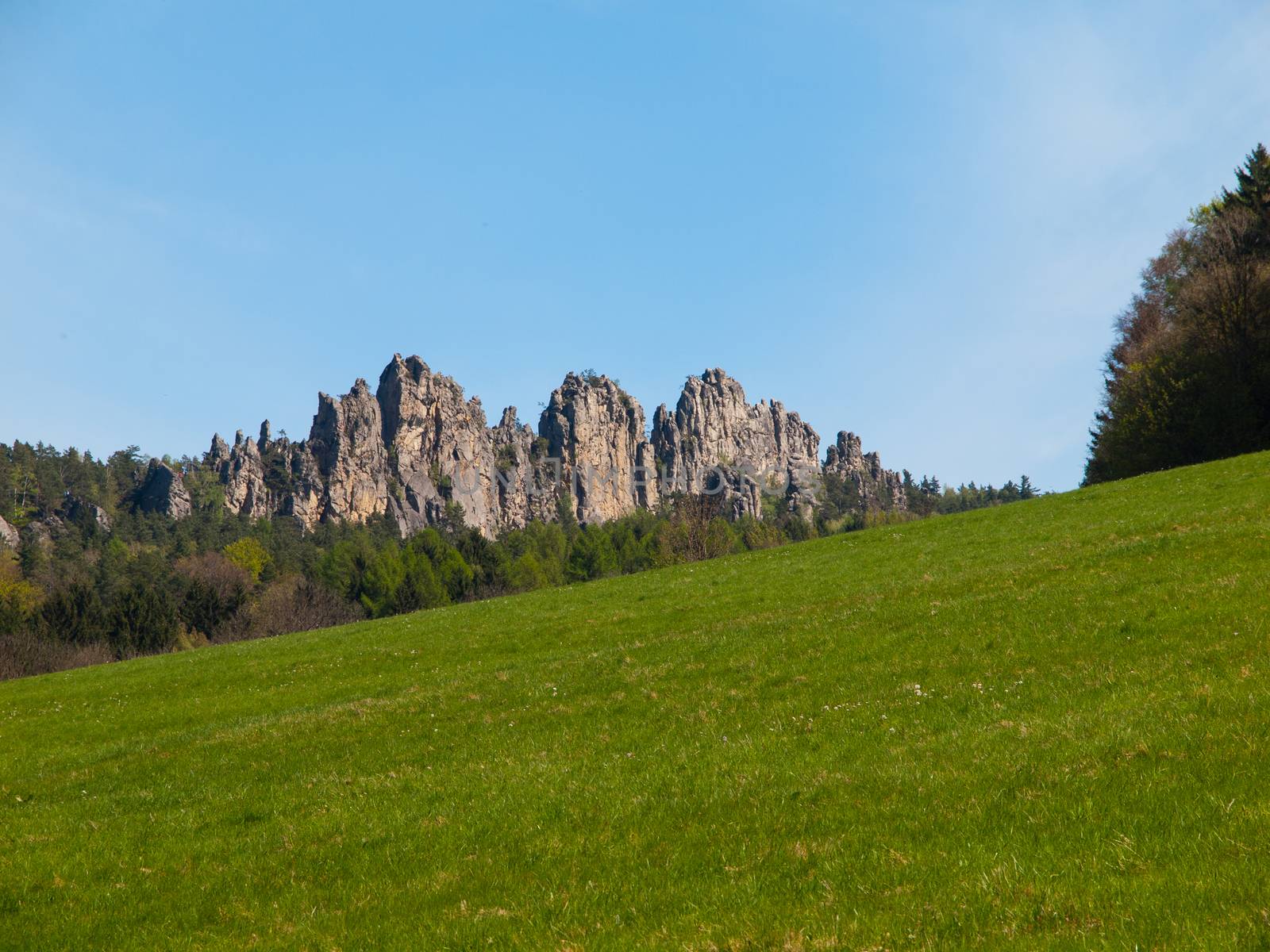 Sharp sand stone rock formation with green meadow and blue sky