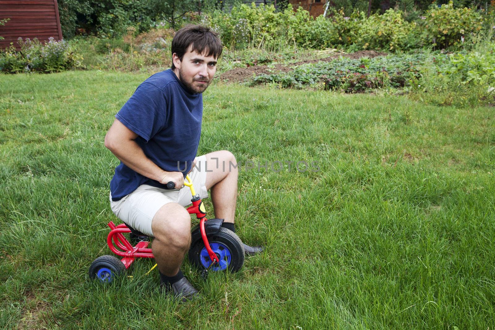 Adult man tying to ride on a small tricycle