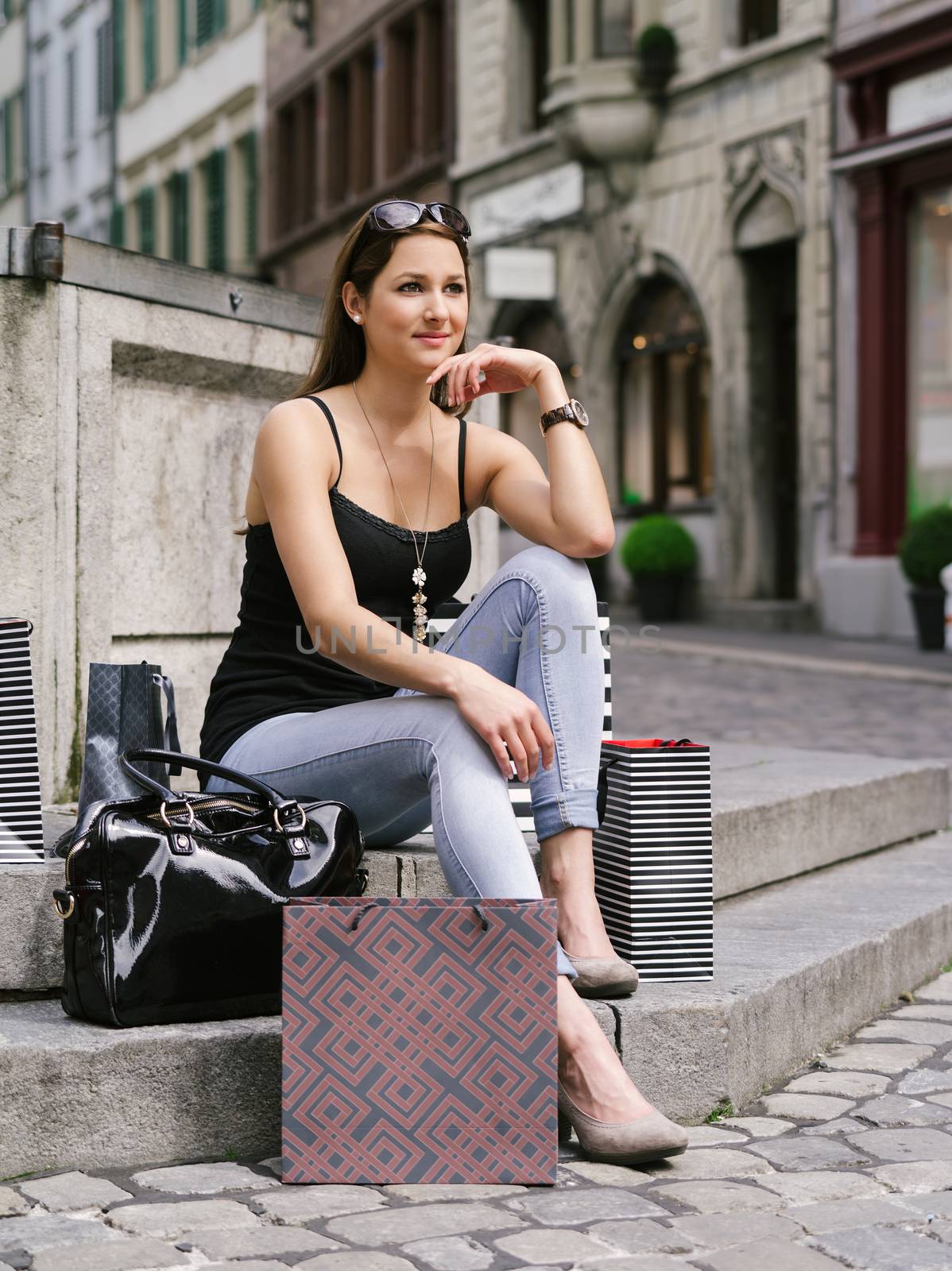 Photo of a beautiful young woman sitting and resting with her shopping bags at a fountain in an old European city.