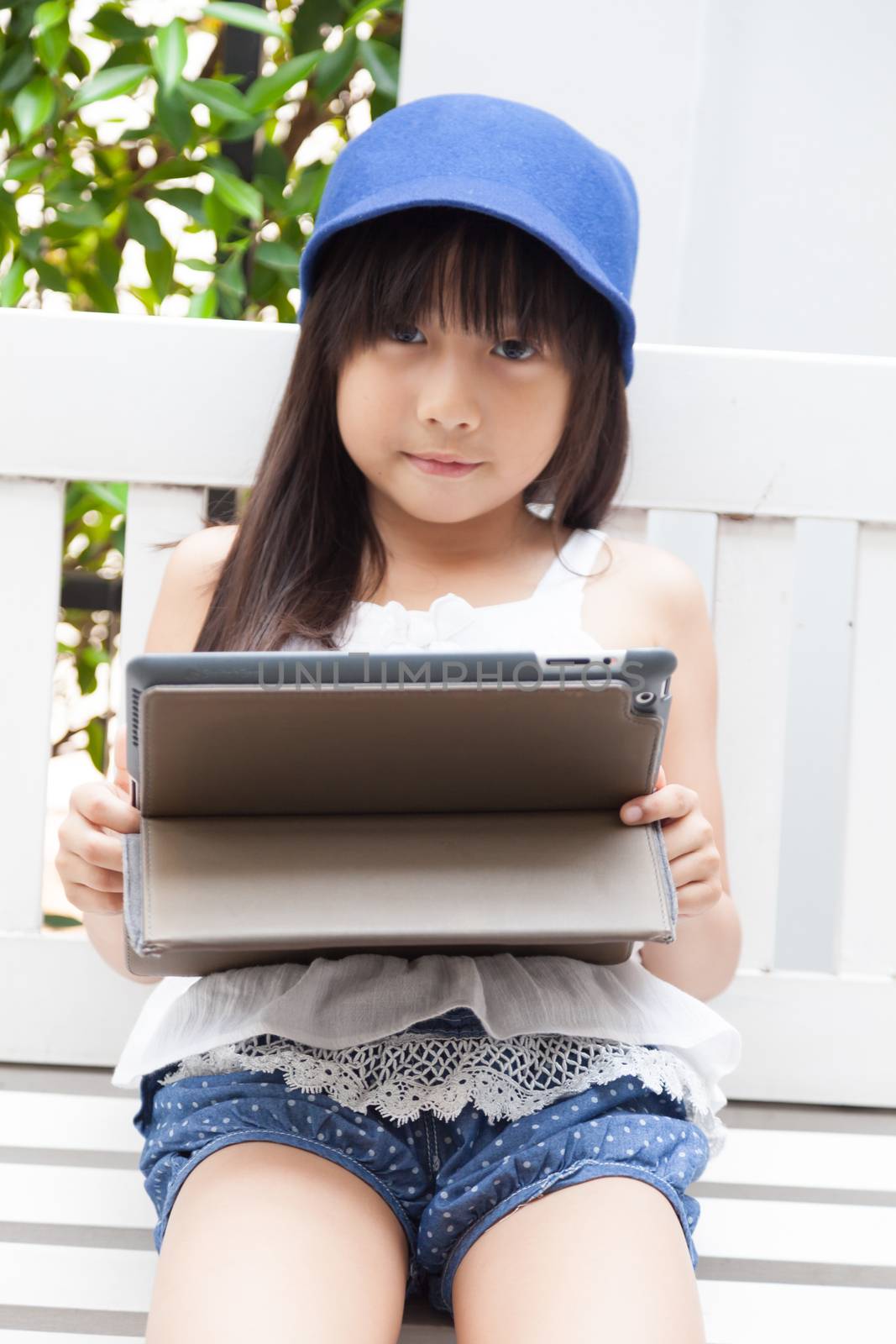 Girl playing with tablet on bench. by a454