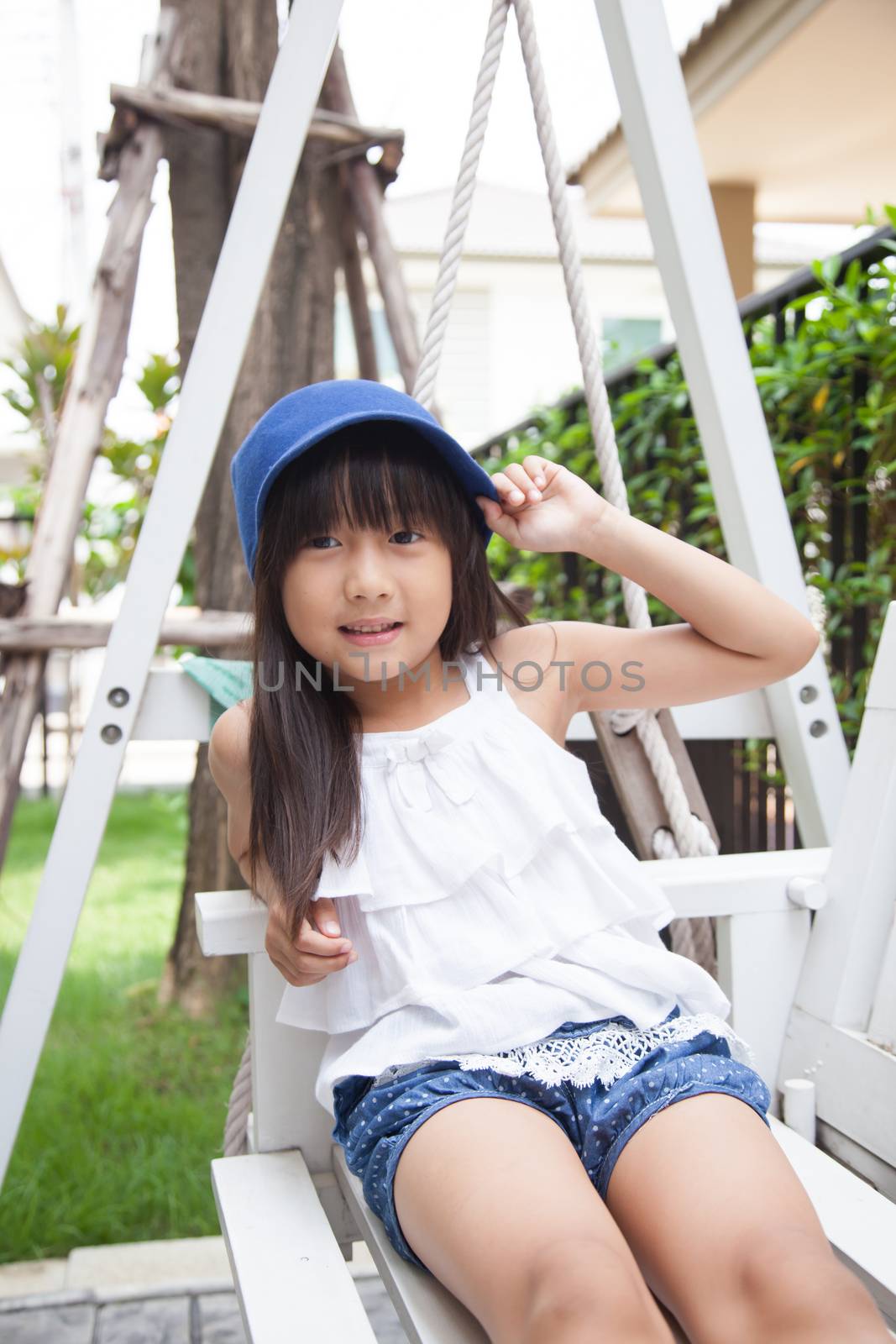 girl sitting on a swing. hand holding blue hat. Smiling and laughing