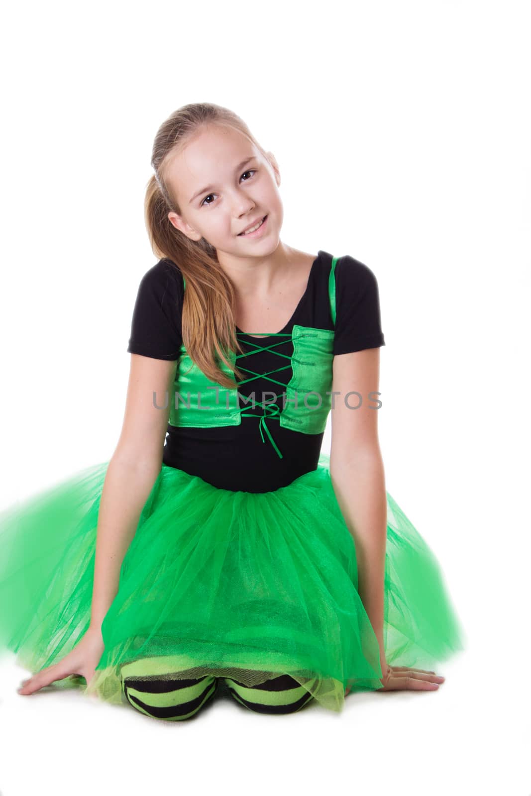 Smiling dancer girl in green tutu skirt sitting isolated on white