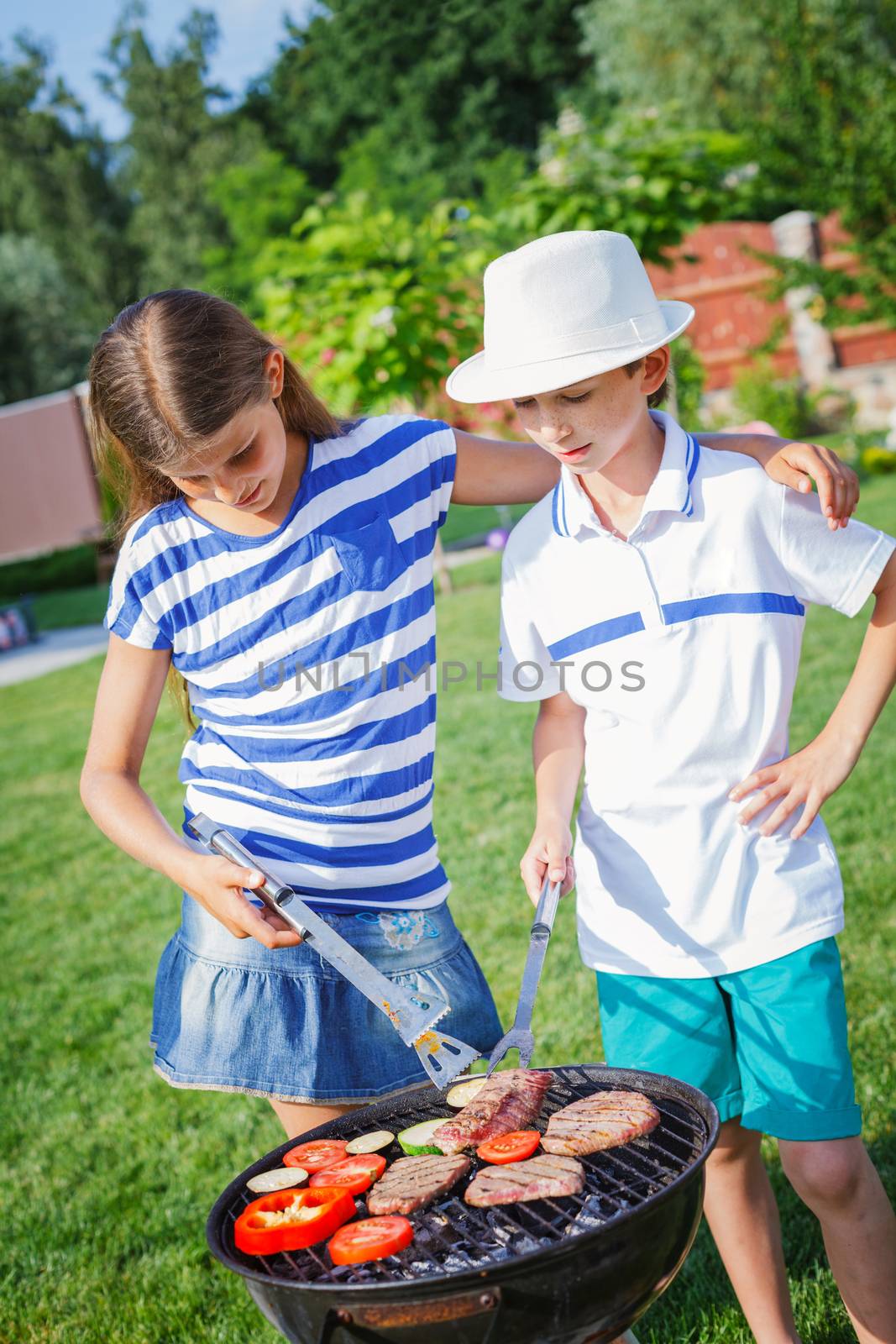 Happy kids preparing meat and vegetables using a barbecue grill