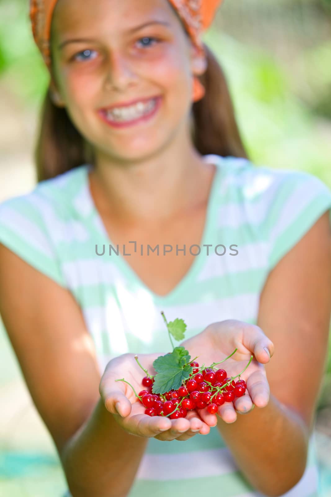 Happy cute girl in summer garden with ripe fresh redcurrant. Focus on the hand.