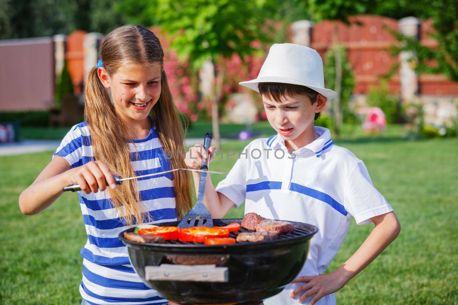 Happy kids preparing meat and vegetables using a barbecue grill