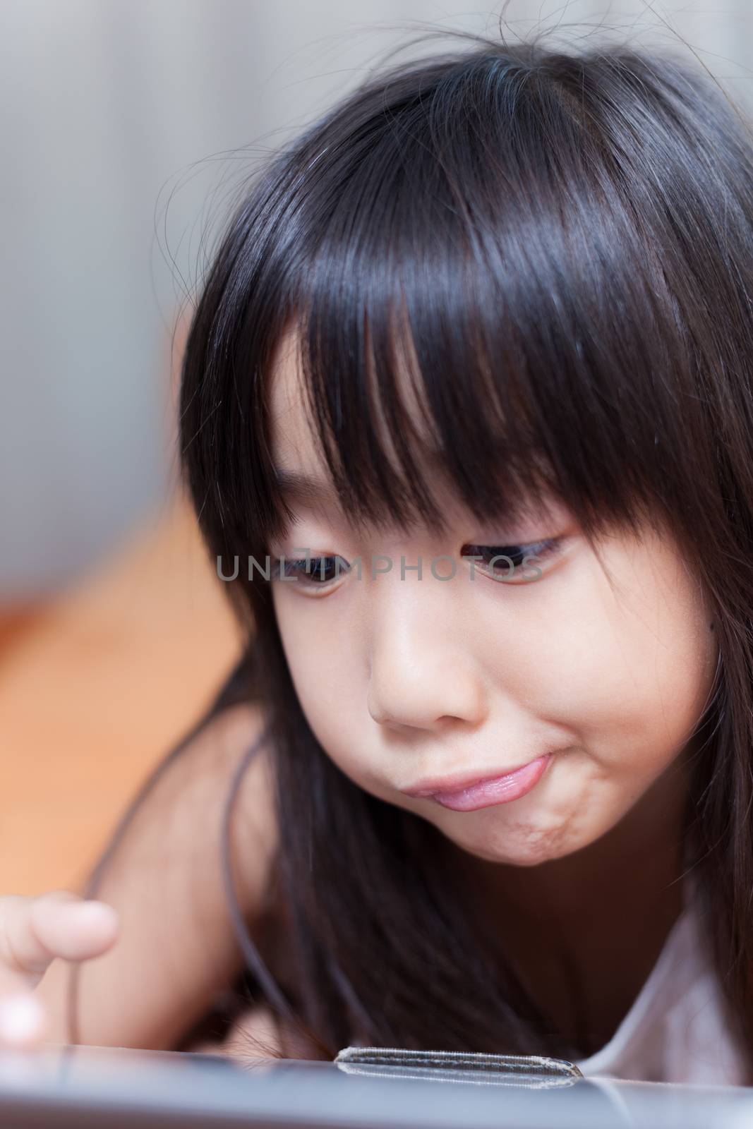 Girl playing with tablet. Played on the orange sofa. Gestures are funny and happy.