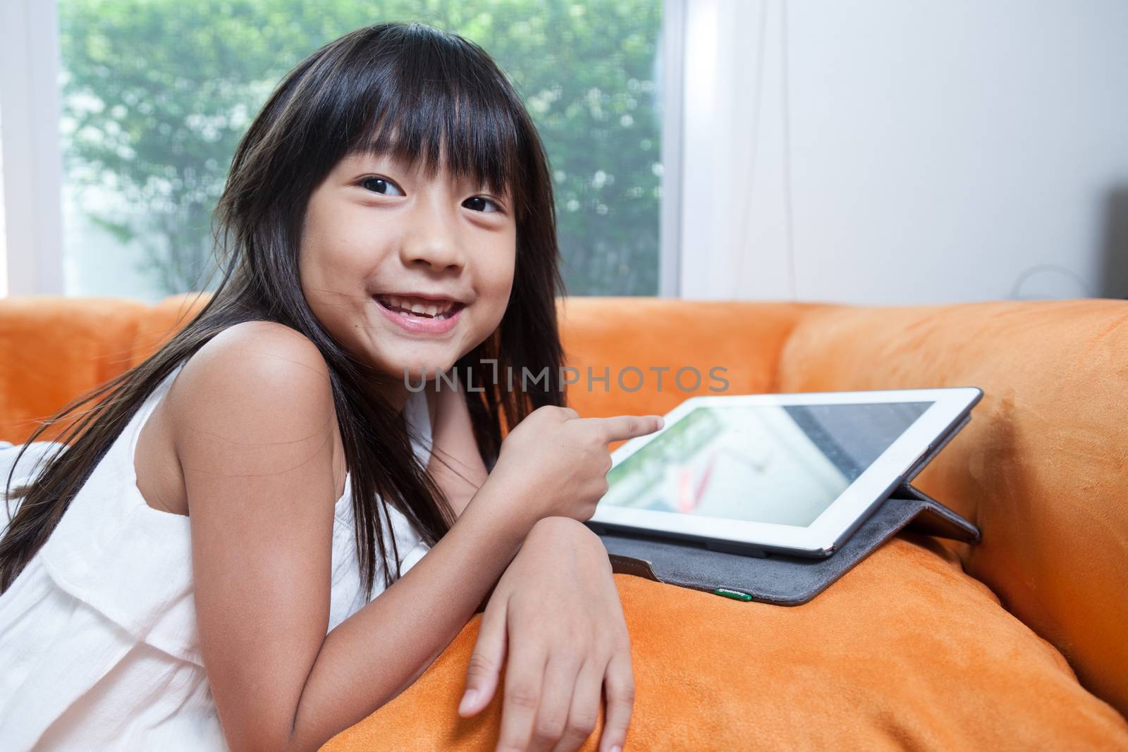 Girl playing with tablet. Lying on the orange sofa at home.girl smiling.