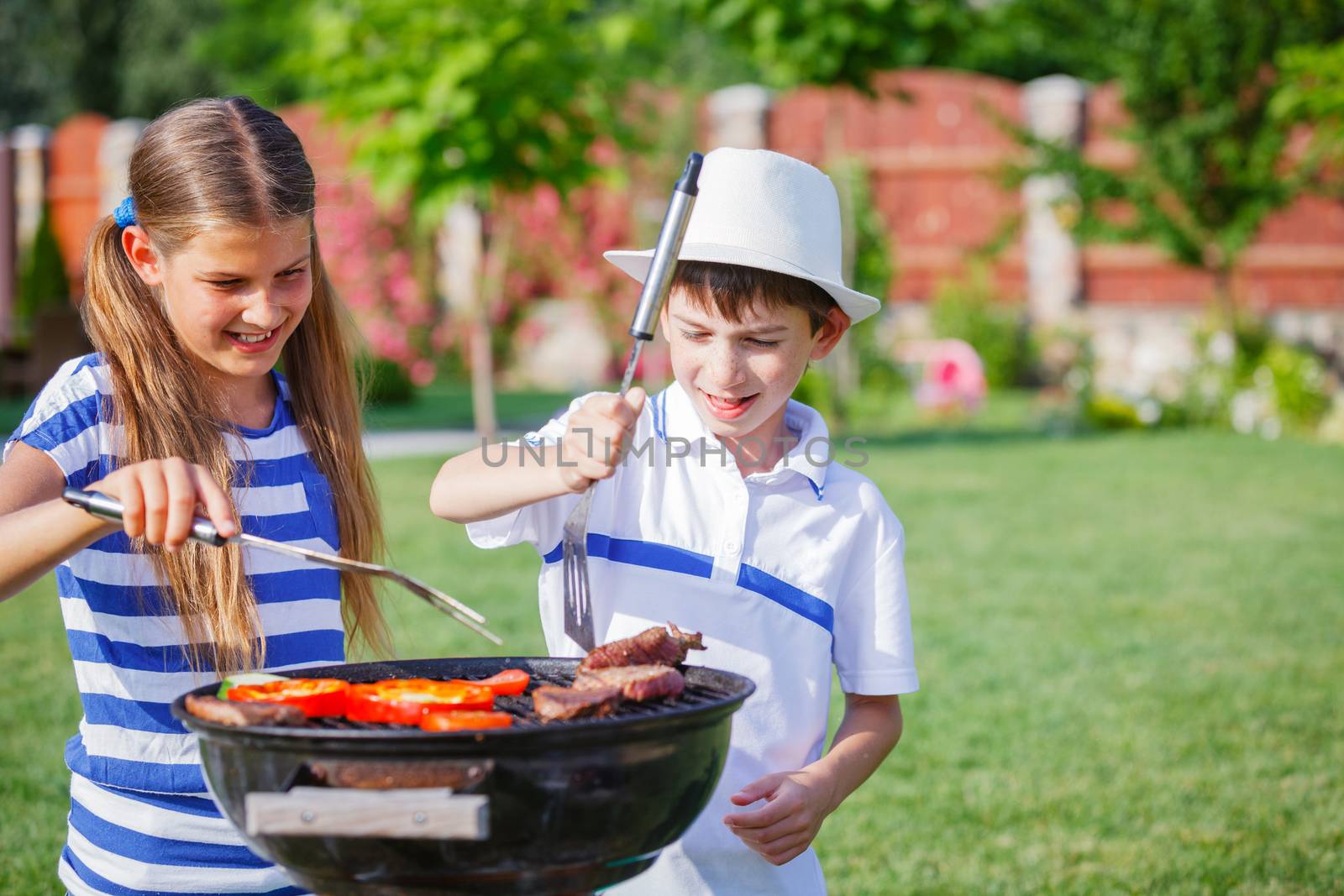 Happy kids preparing meat and vegetables using a barbecue grill