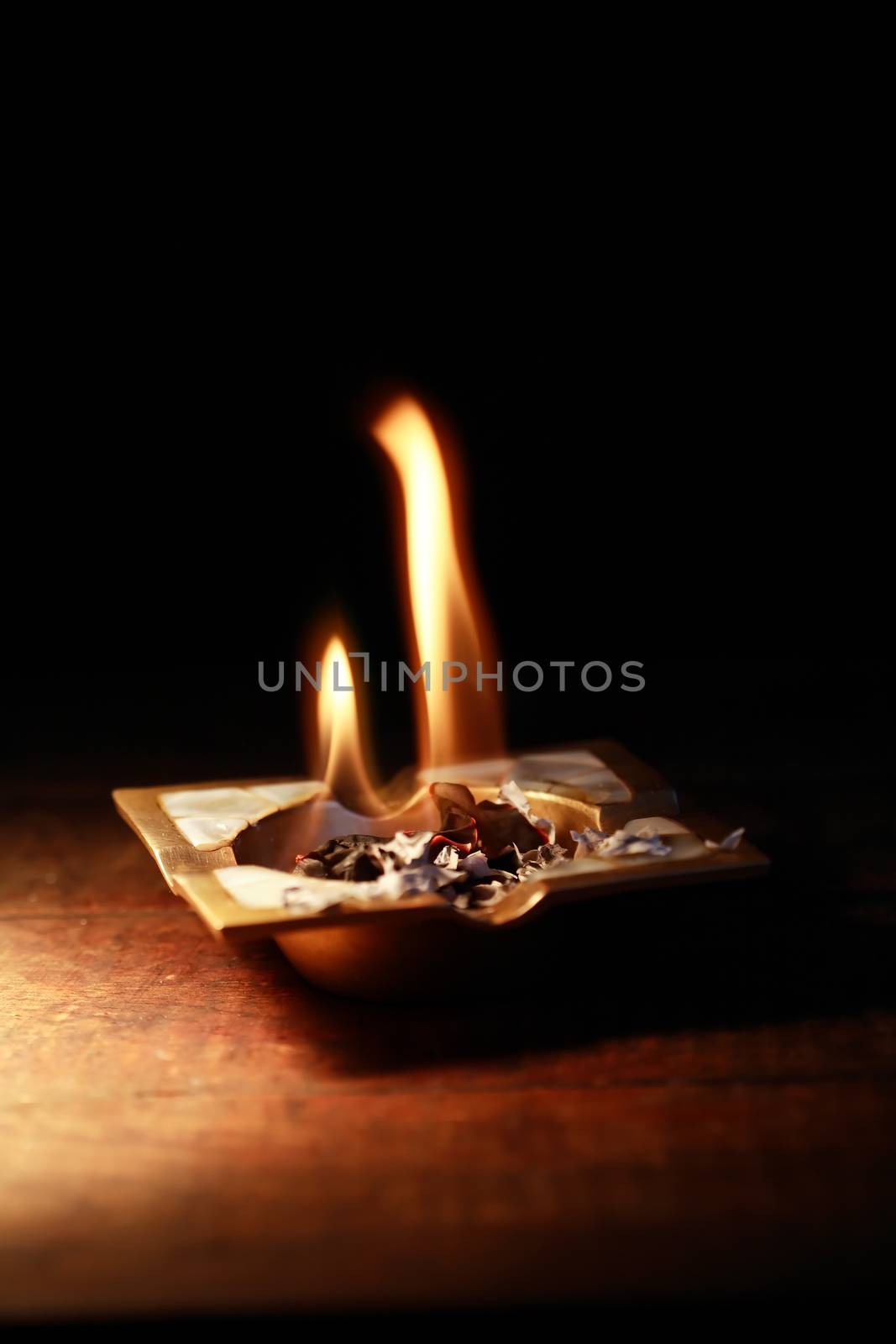 Burning paper in vintage ashtray on dark background