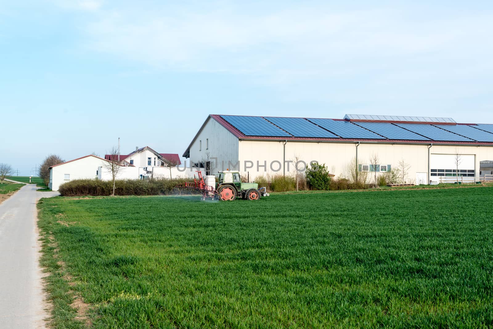 an agricultural tractor starts a chemical treatment run across new growing crops in front of a large farm, with copy space below.