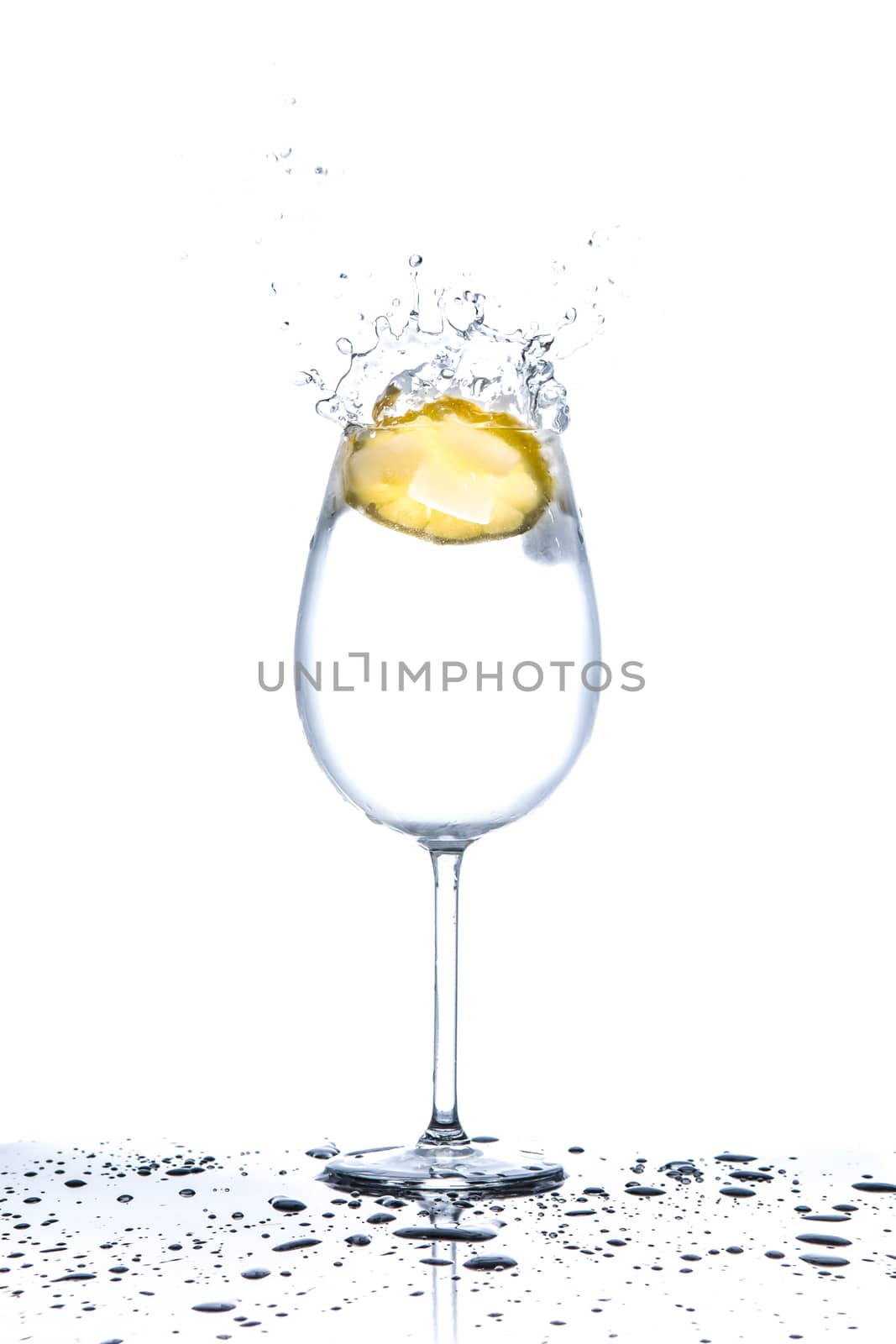 Lemon splashing into glass of water on white background by martinm303