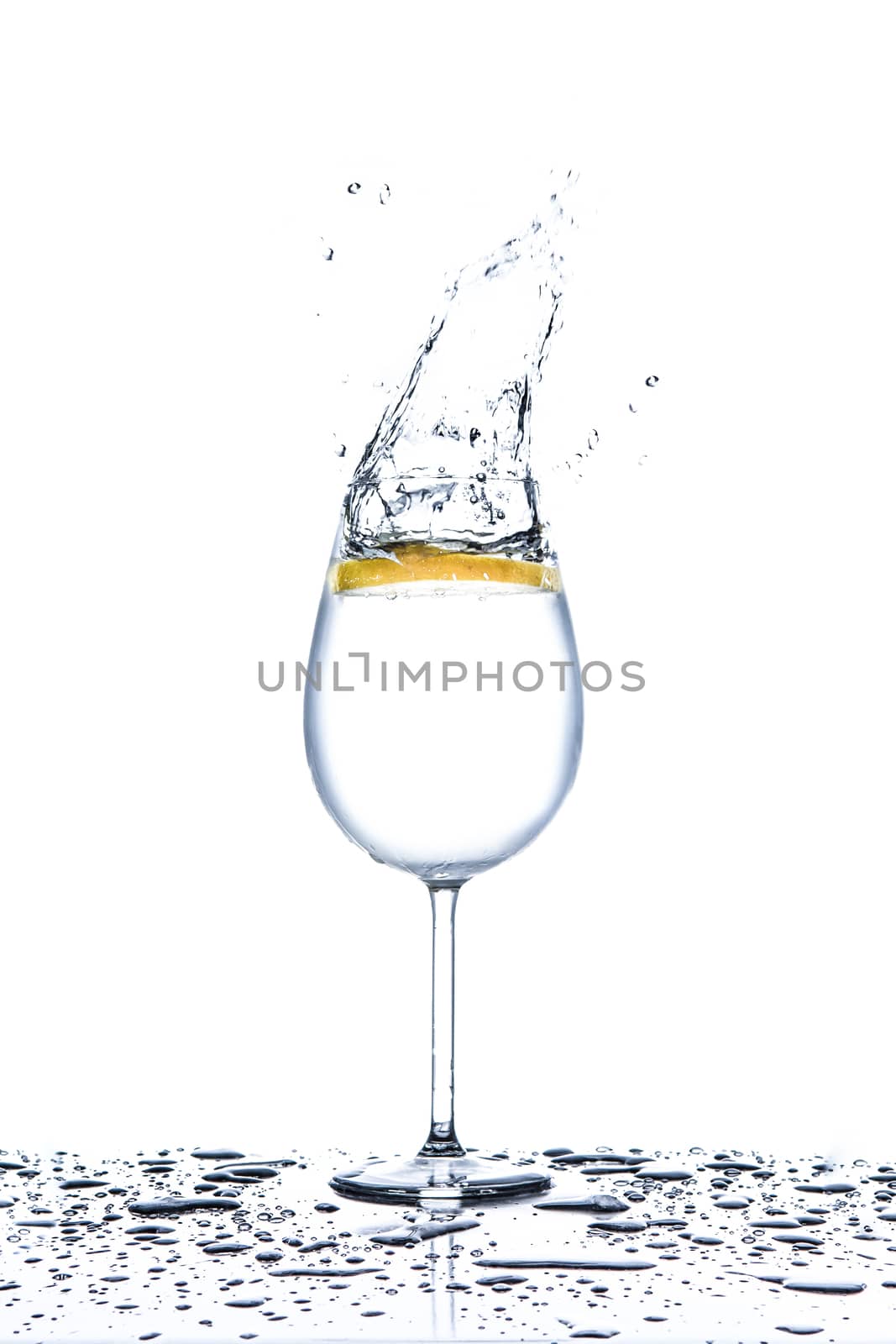 Lemon splashing into glass of water on white background by martinm303