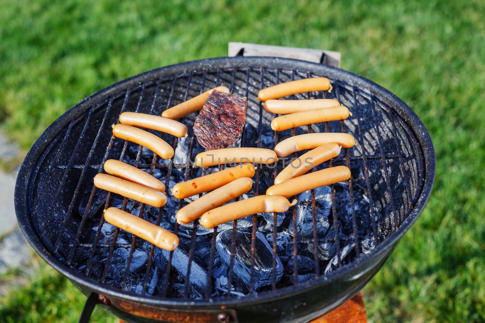 Fresh sausage and hot dogs grilling outdoors on a barbecue grill.