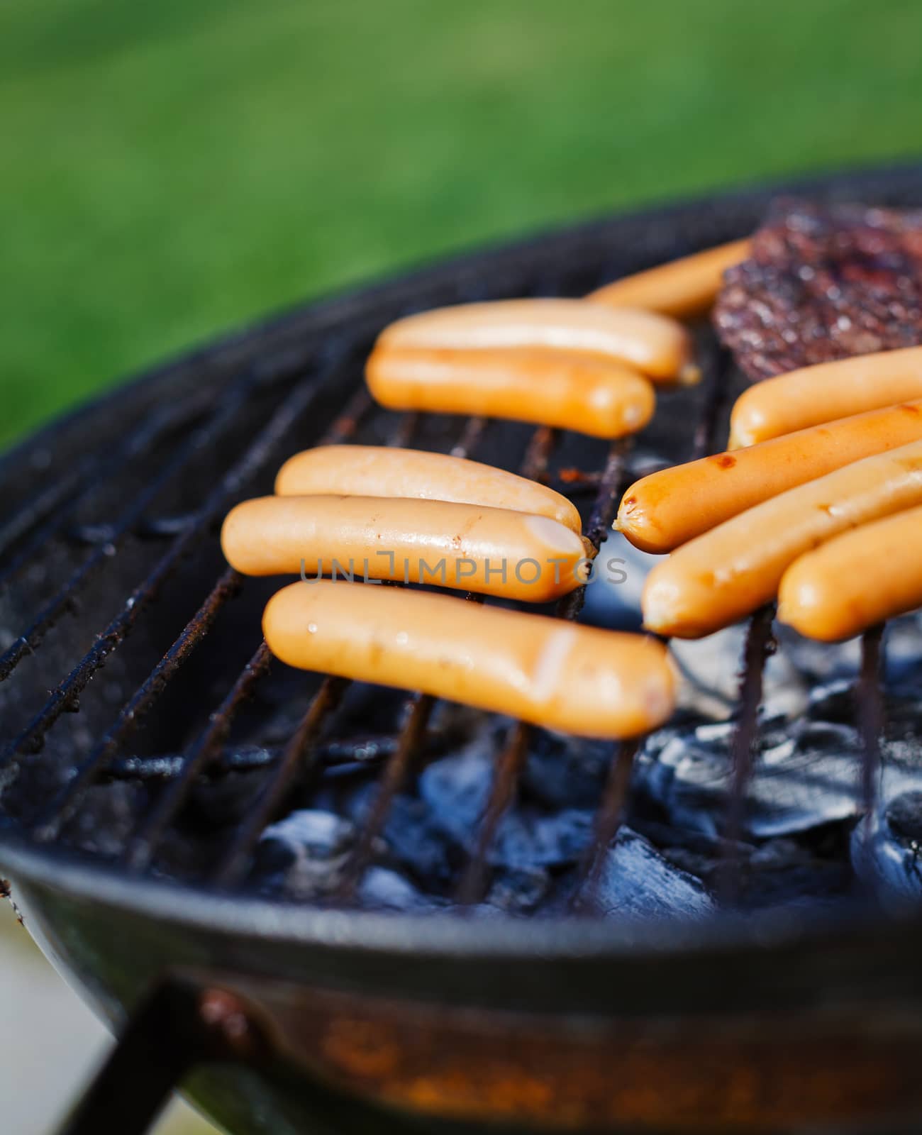 Fresh sausage and hot dogs grilling outdoors on a barbecue grill.