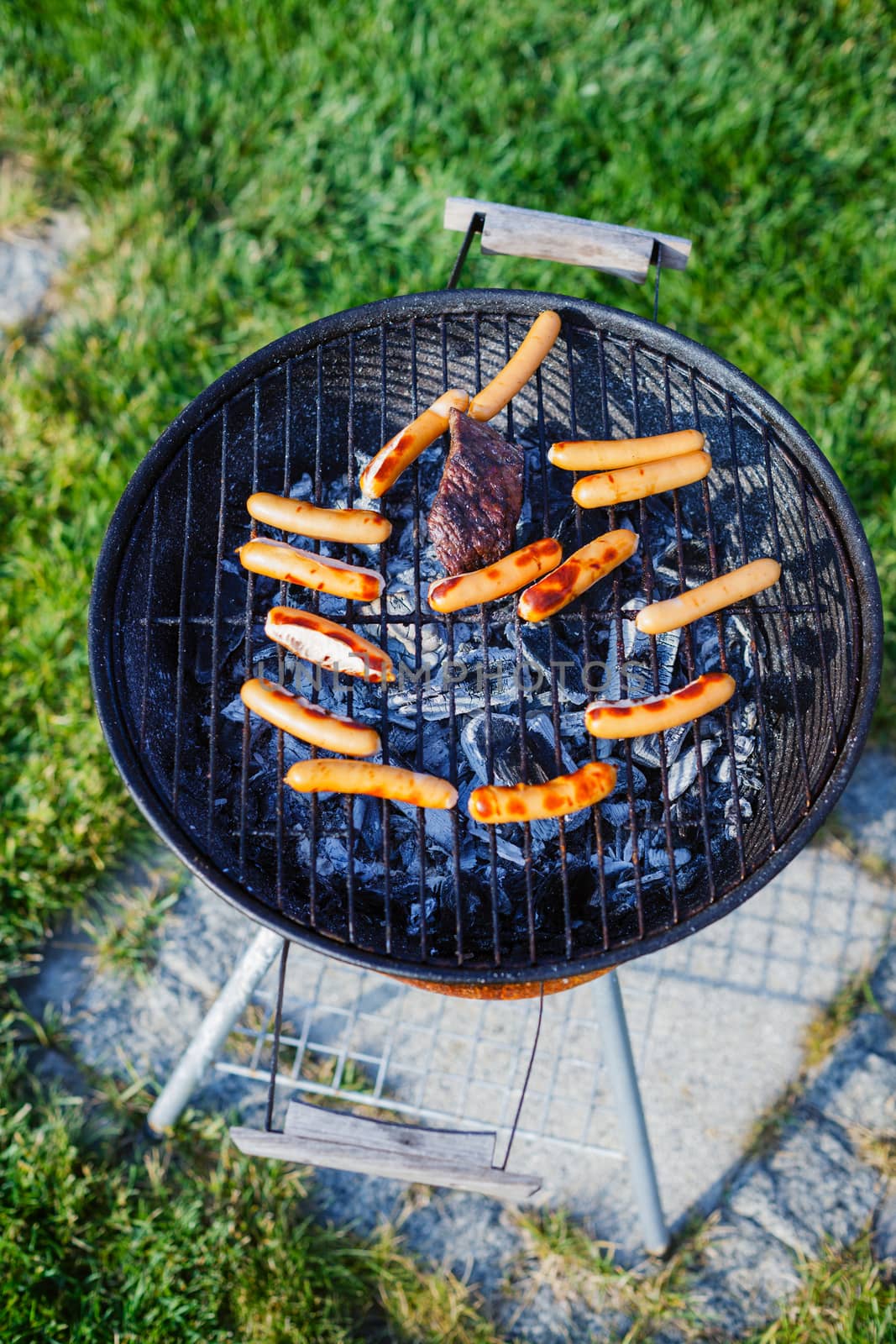 Fresh sausage and hot dogs grilling outdoors on a barbecue grill.