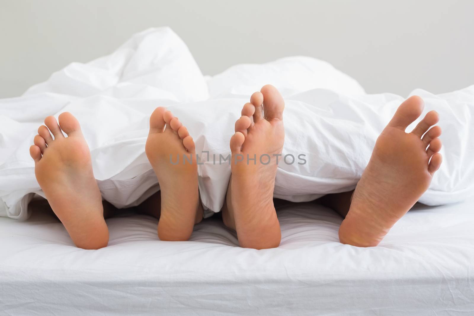 Couples feet sticking out from under duvet at home in bedroom