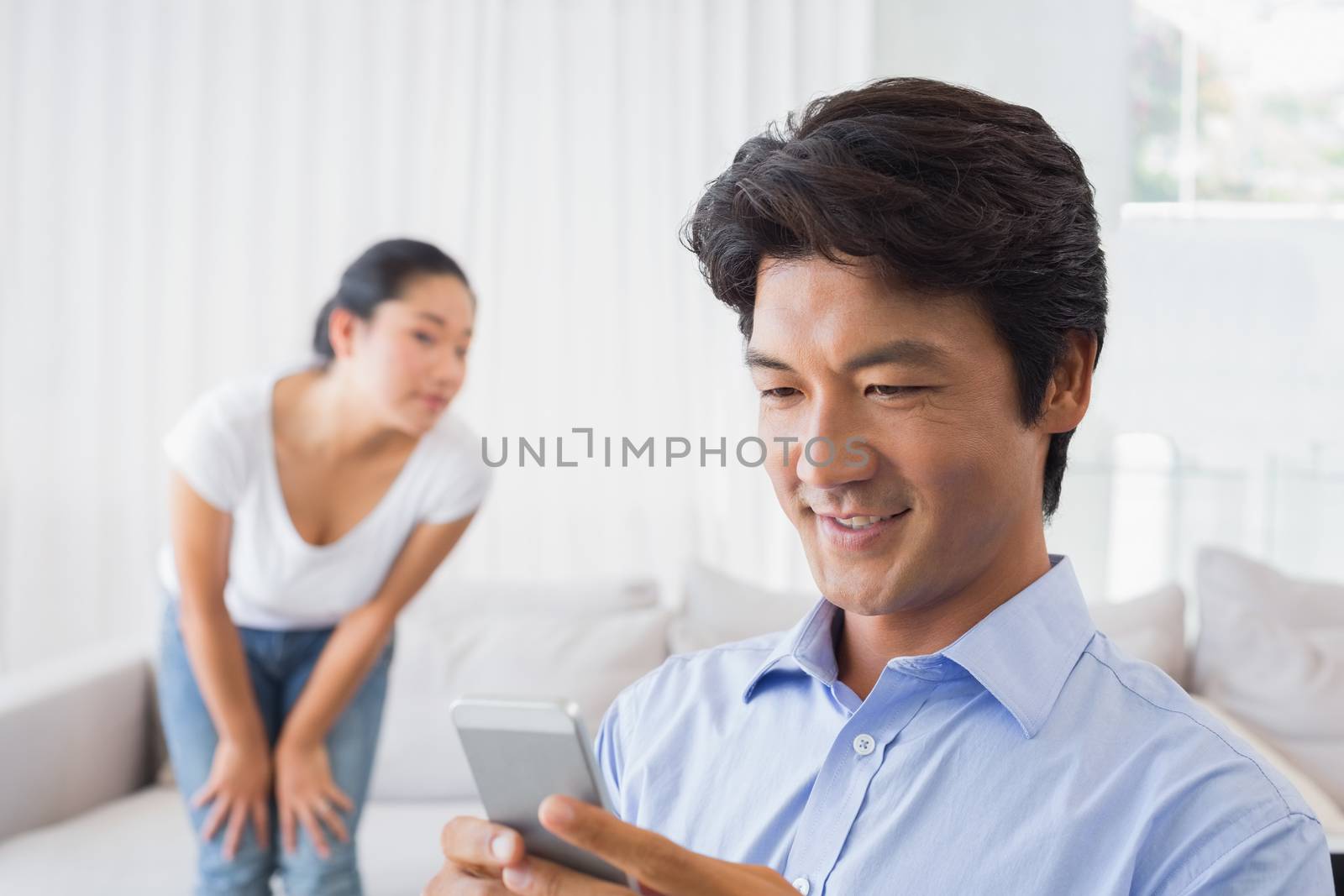 Man sending a text while girlfriend watches from couch at home in the living room
