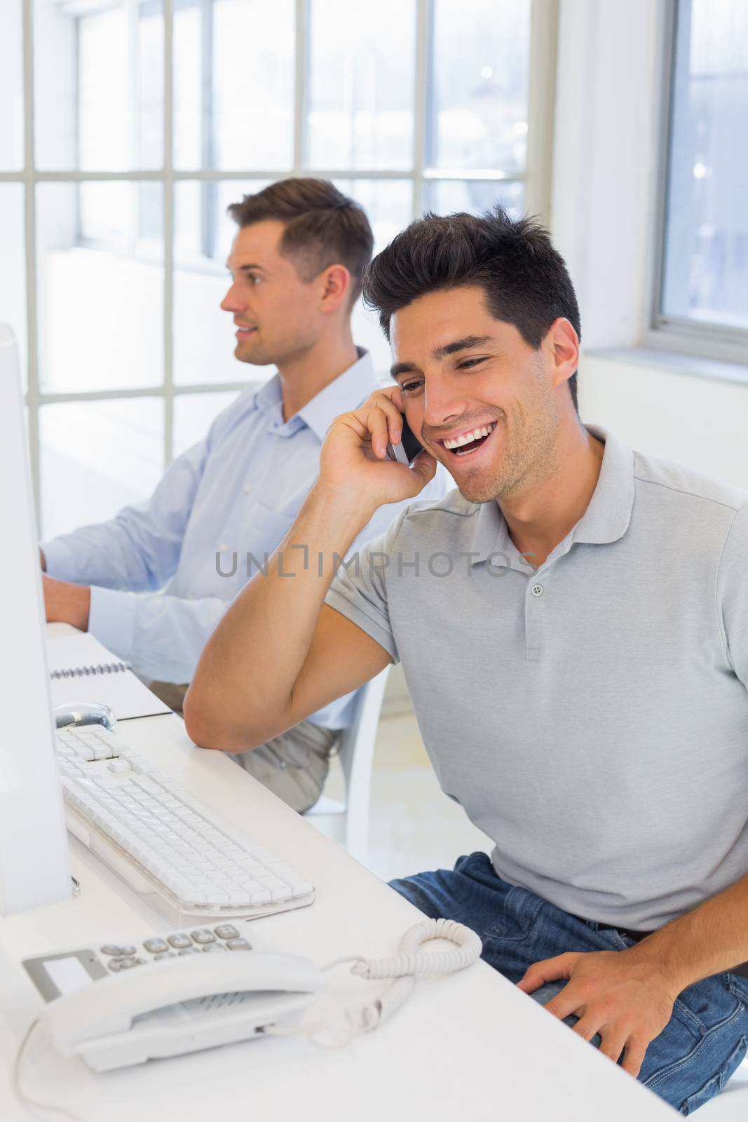 Casual businessman laughing on the phone at his desk in the office