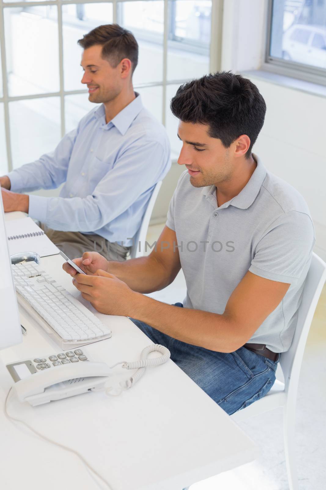 Casual businessman sending a text at his desk by Wavebreakmedia
