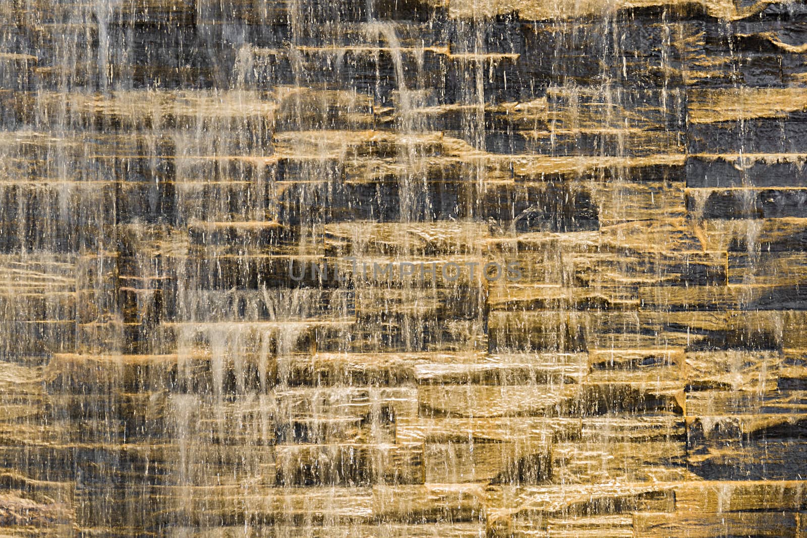 Falling water stream against stonework rough texture with night backlight