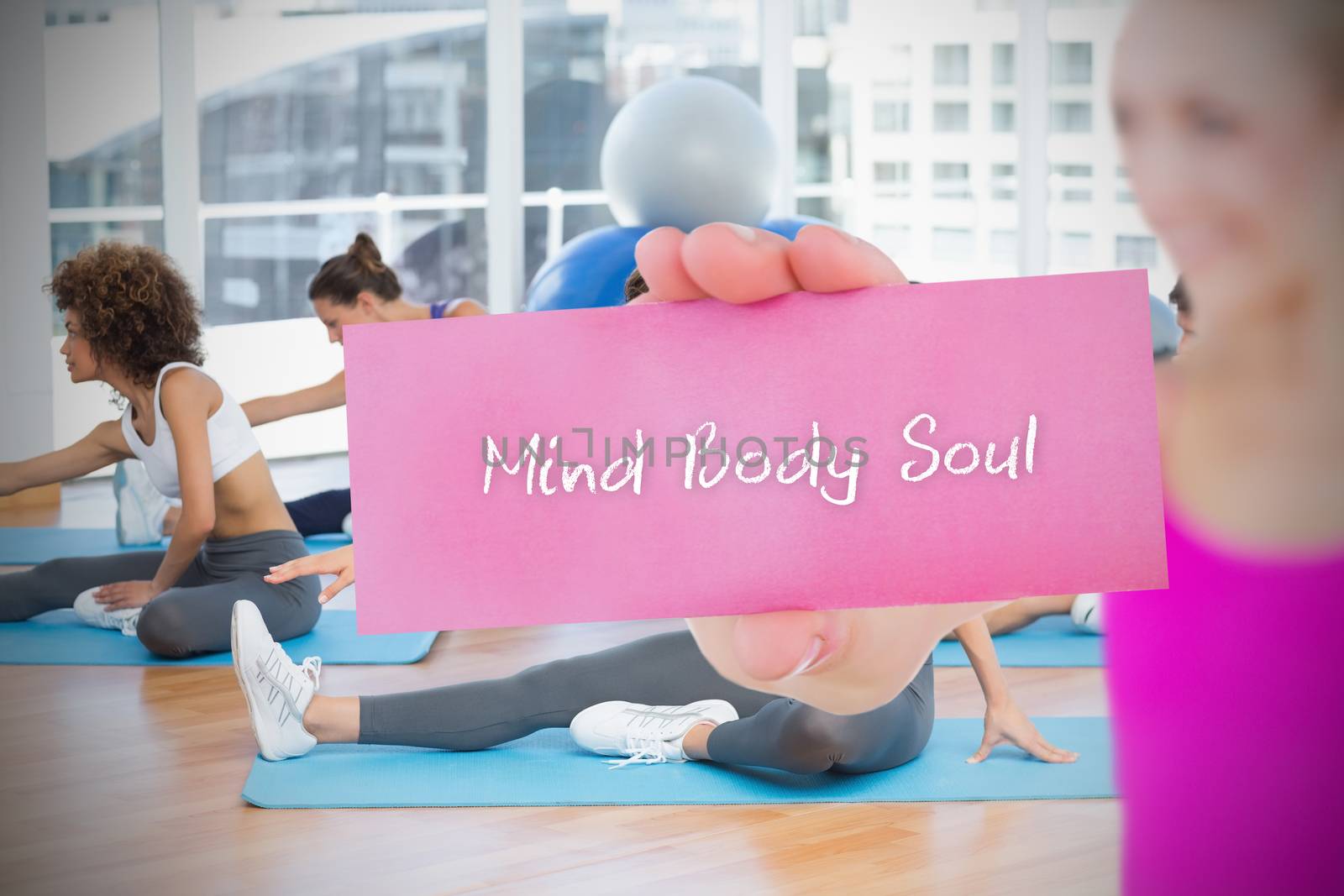 Fit blonde holding card saying mind body soul against yoga class in gym 