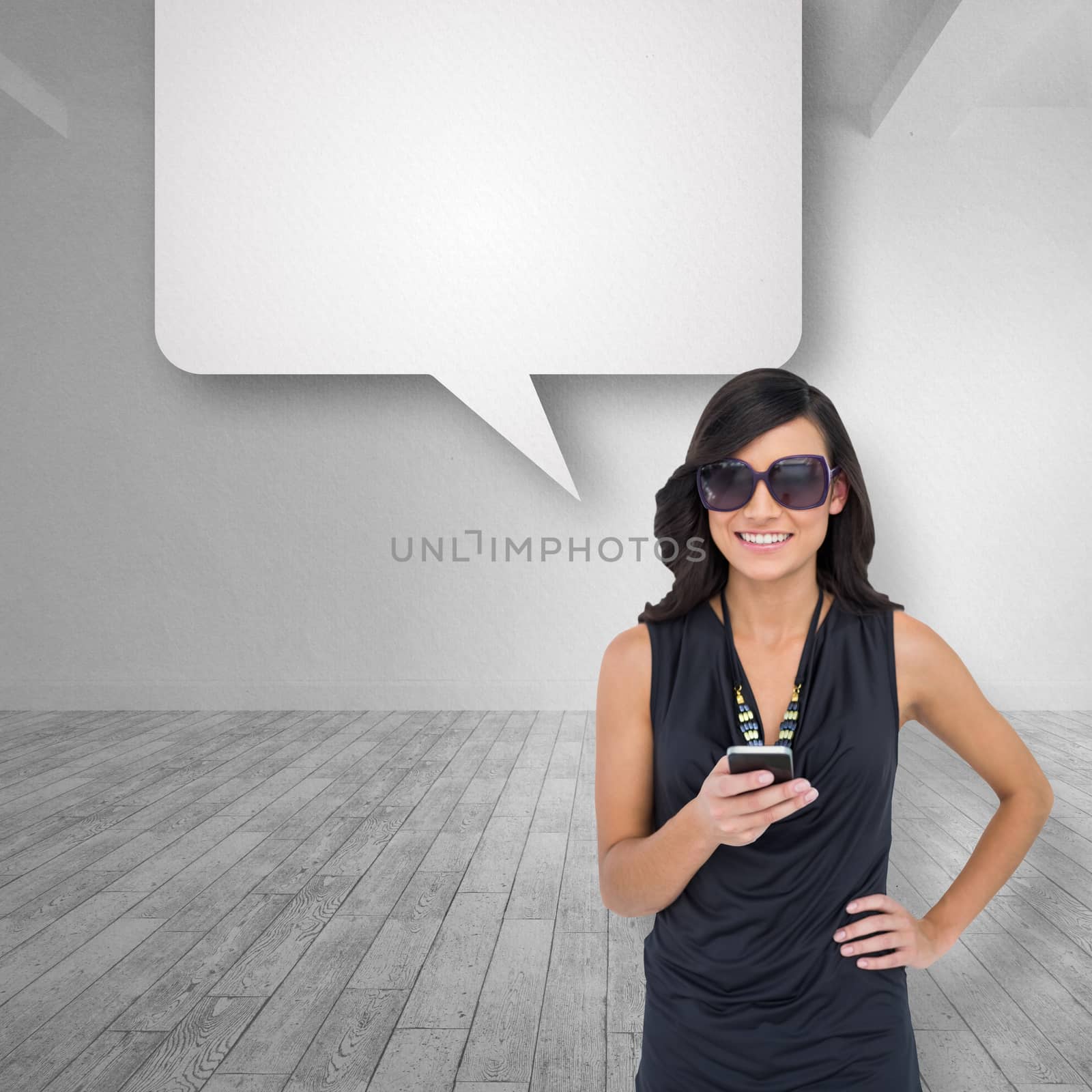 Happy brunette holding smartphone against bright white room with speech bubble