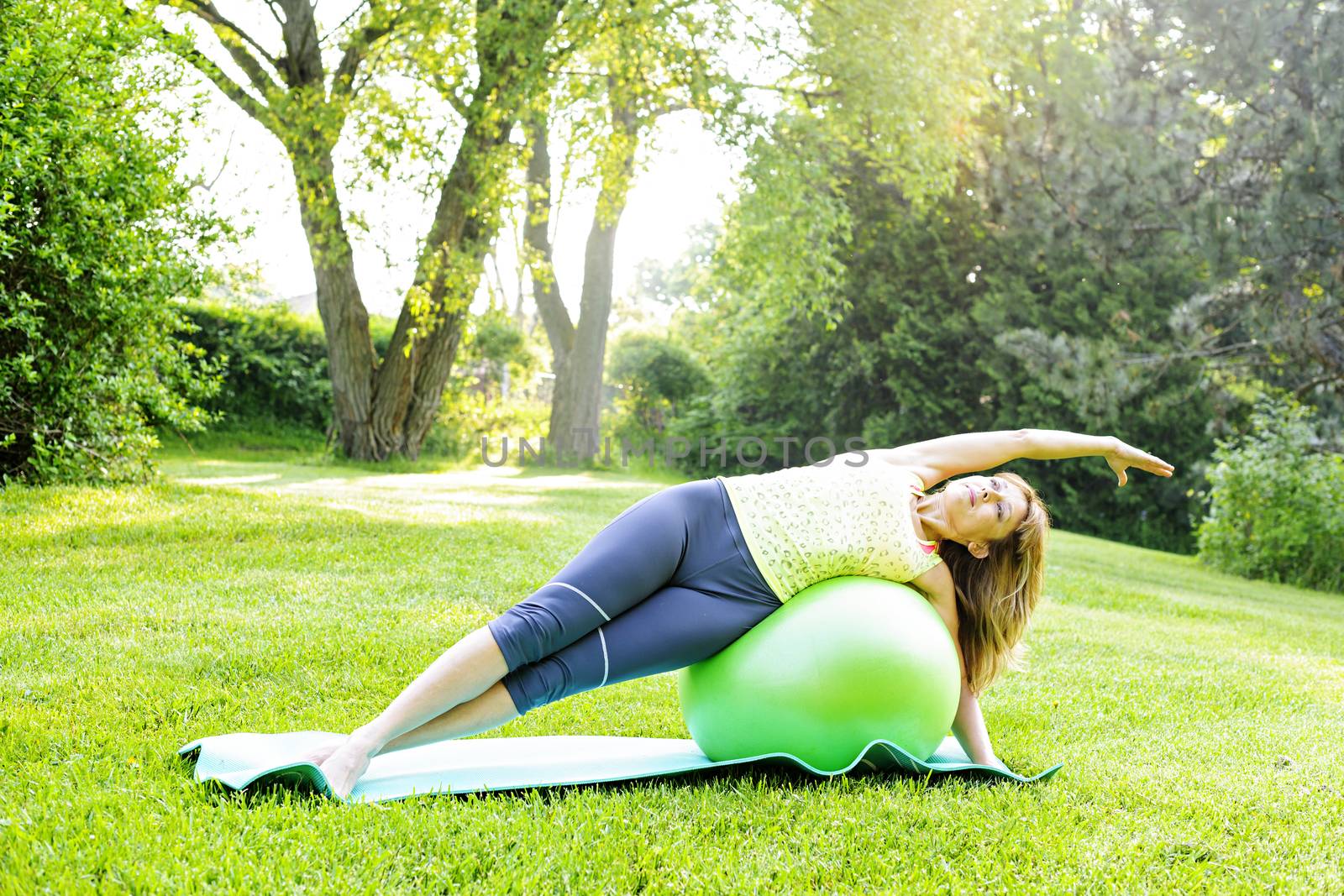 Female fitness instructor using yoga exercise ball in green park