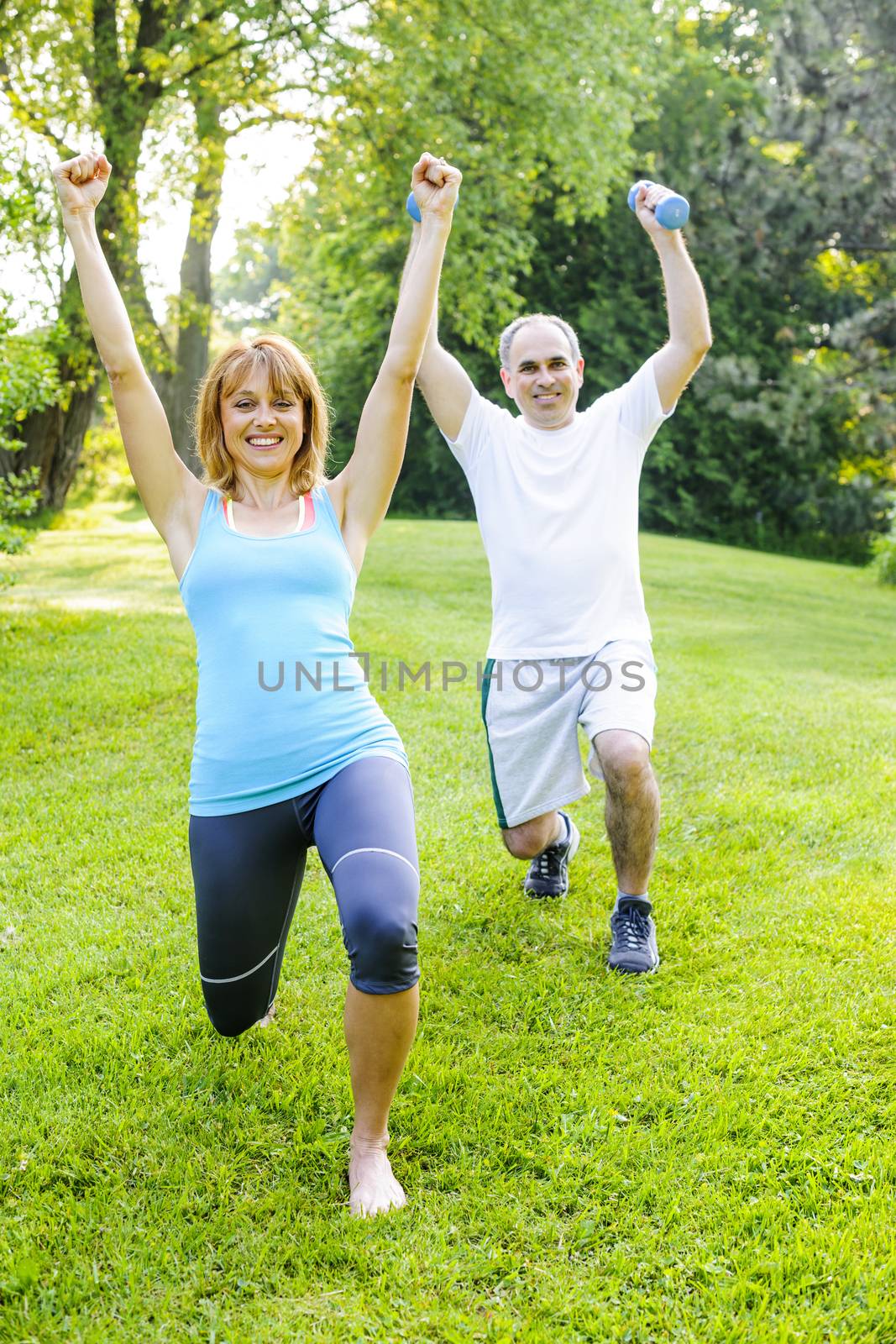 Female fitness instructor exercising with middle aged man in green park