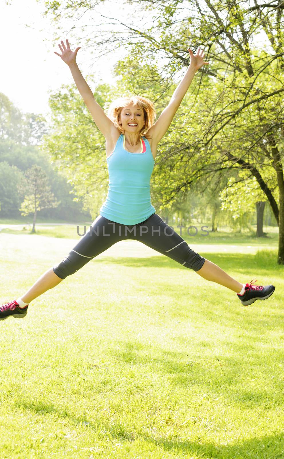 Happy female fitness instructor jumping exercising outside at green park