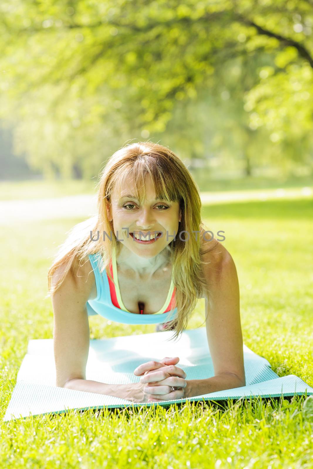 Female fitness instructor holding plank pose exercising outside in green summer park