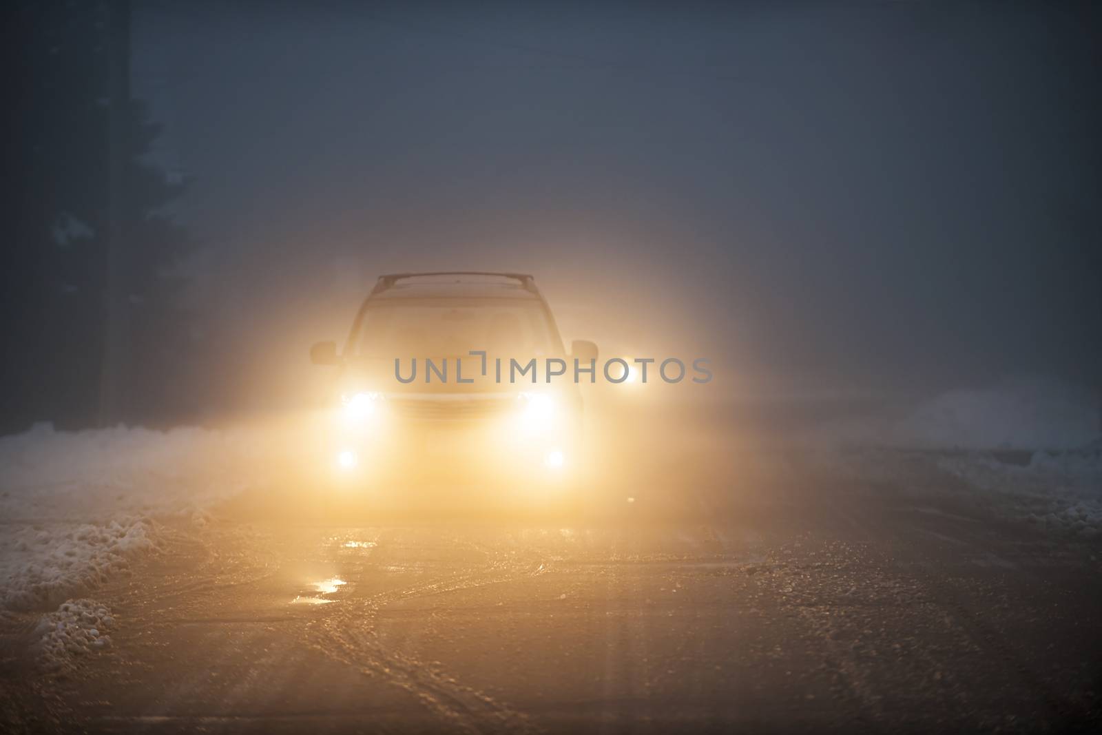 Bright headlights of a car driving on foggy winter road