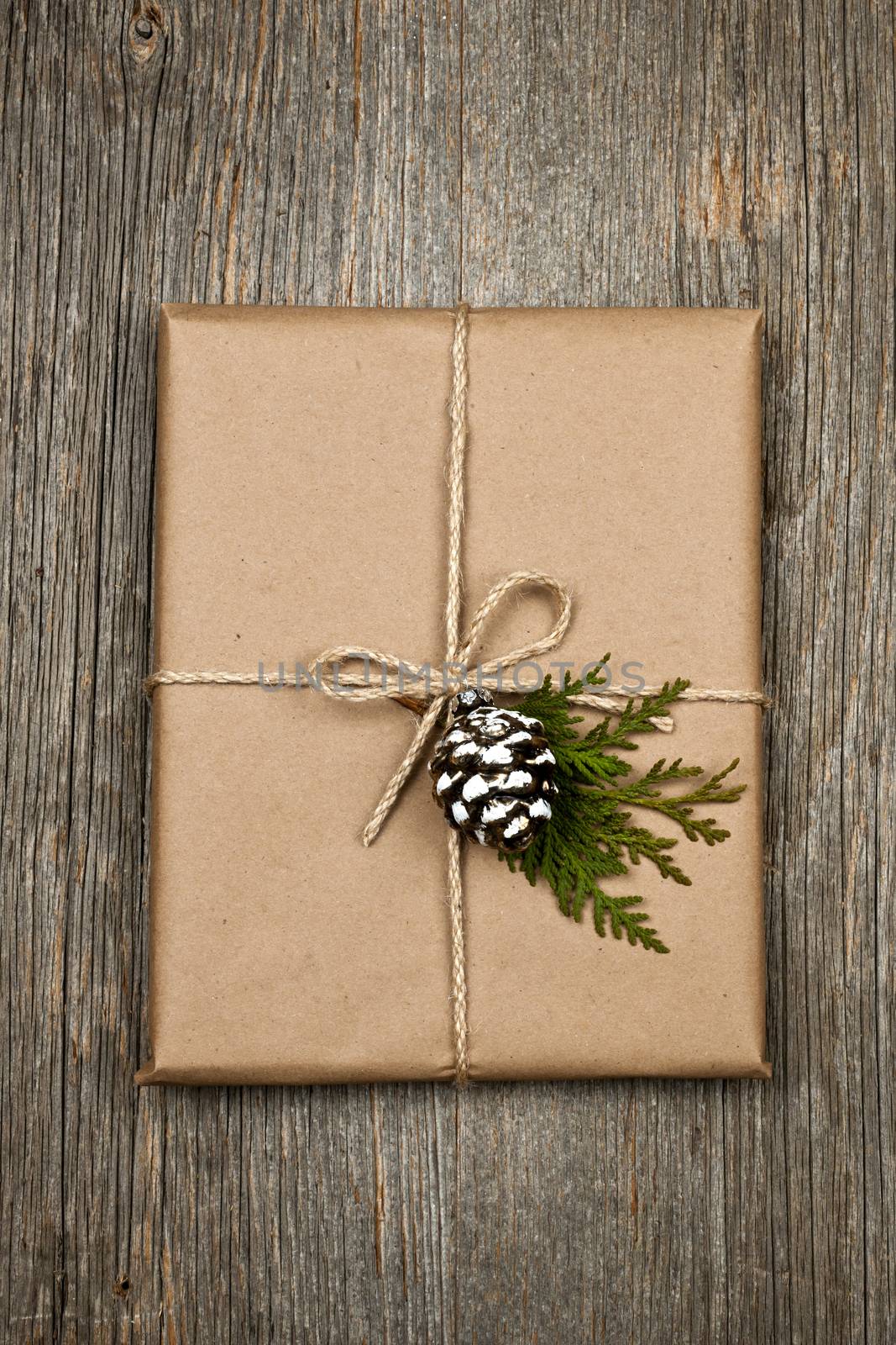 Christmas gift in brown wrapping and string with pine cone decoration on old wood background