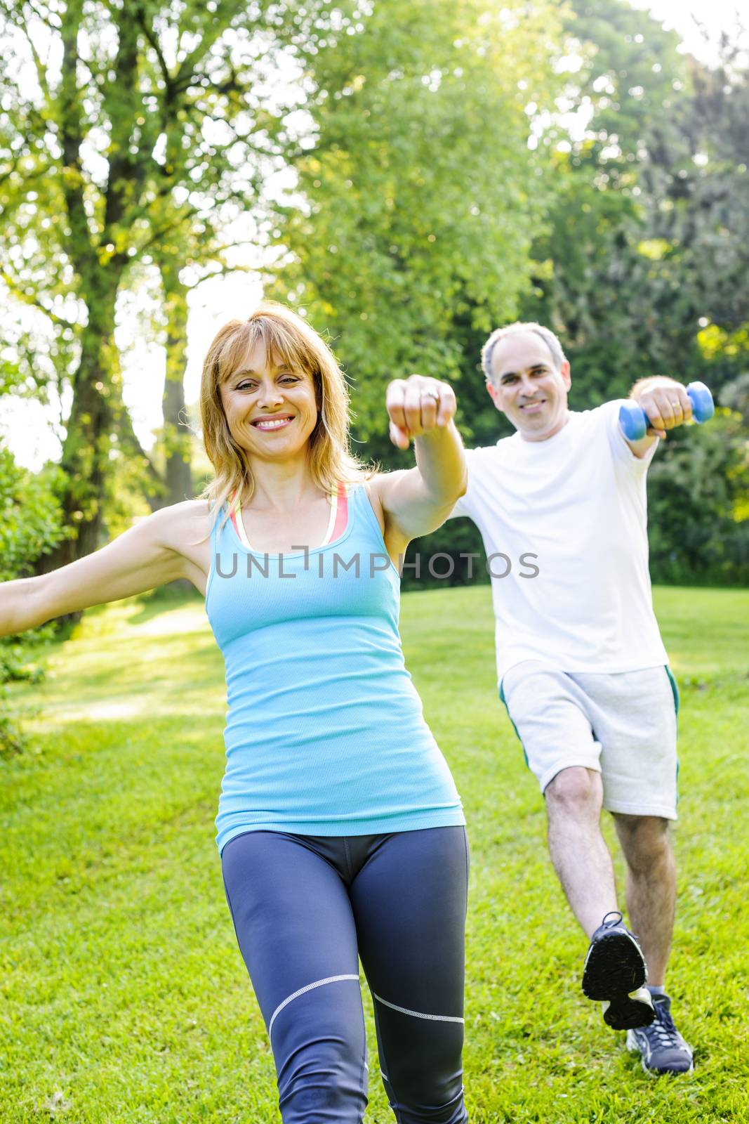 Female fitness instructor exercising with middle aged man outdoors in green park
