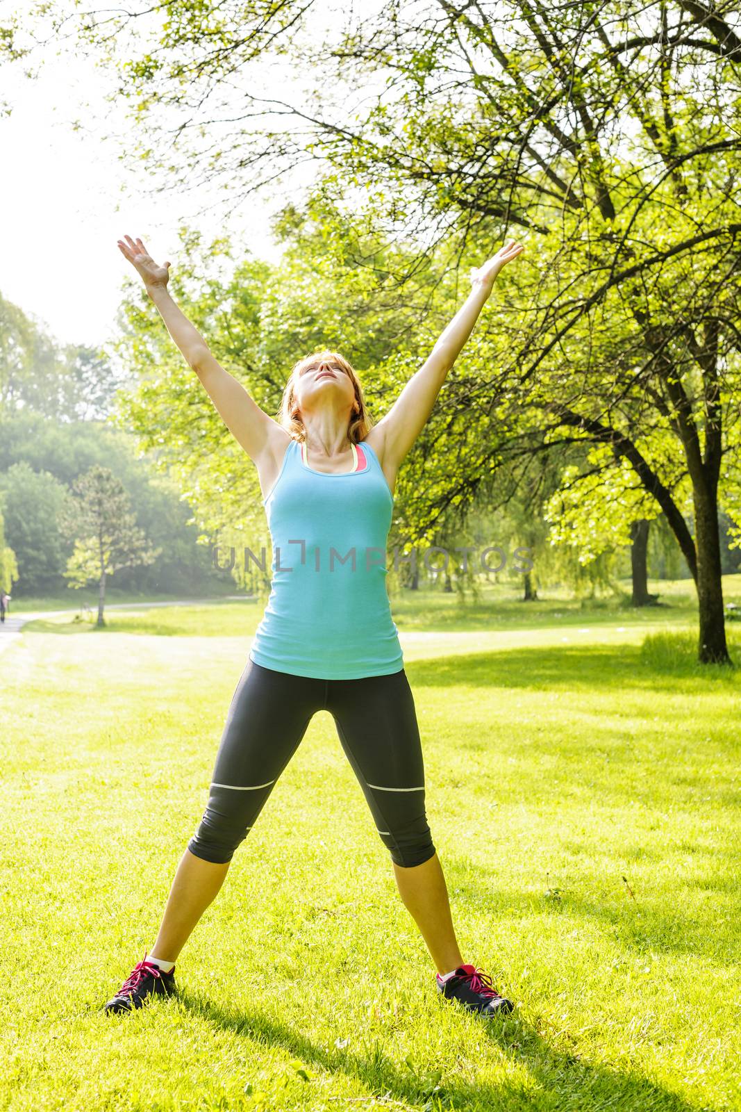 Female fitness instructor stretching at green park in the morning