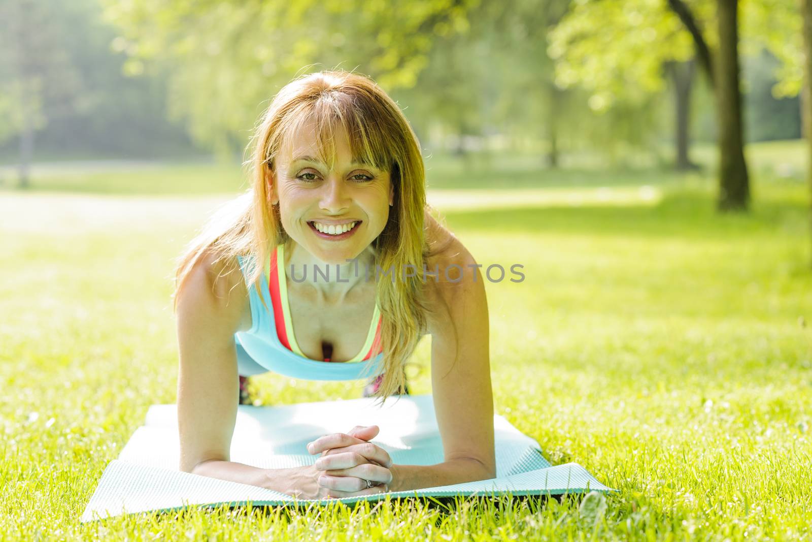 Female fitness instructor holding plank pose exercising outside in green summer park