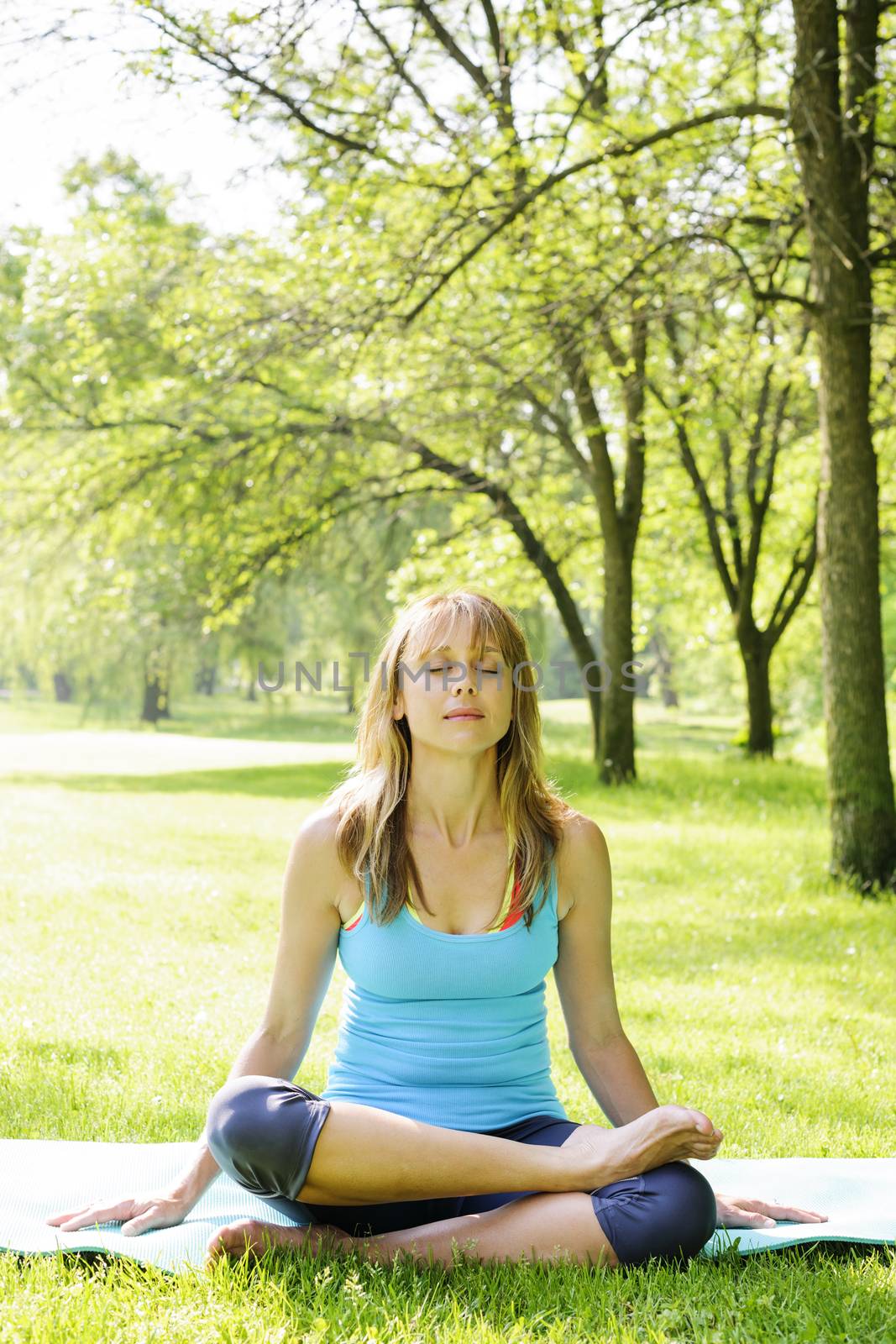 Female fitness instructor in lotus yoga pose outdoor at spring park