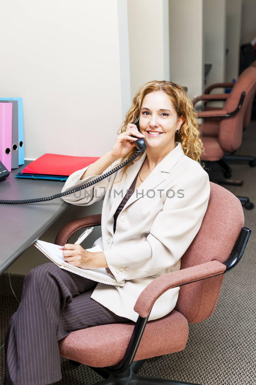 Businesswoman on phone taking notes in office workstation