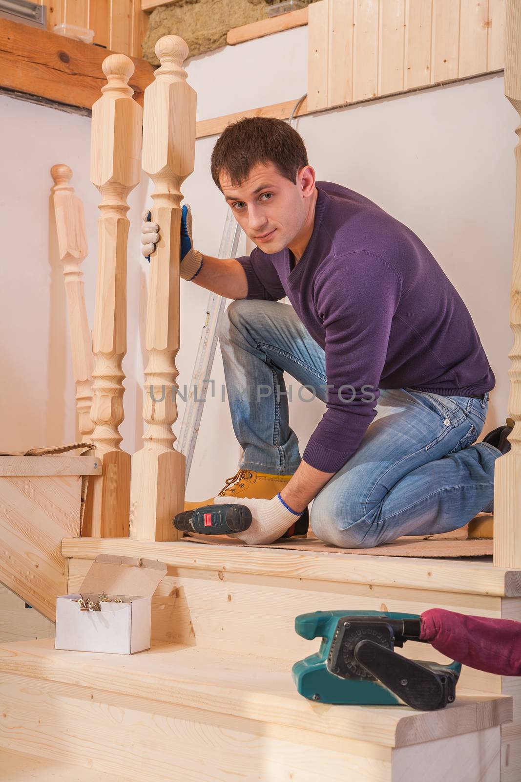 young worker fixing post of wooden  ladder and looking at camera