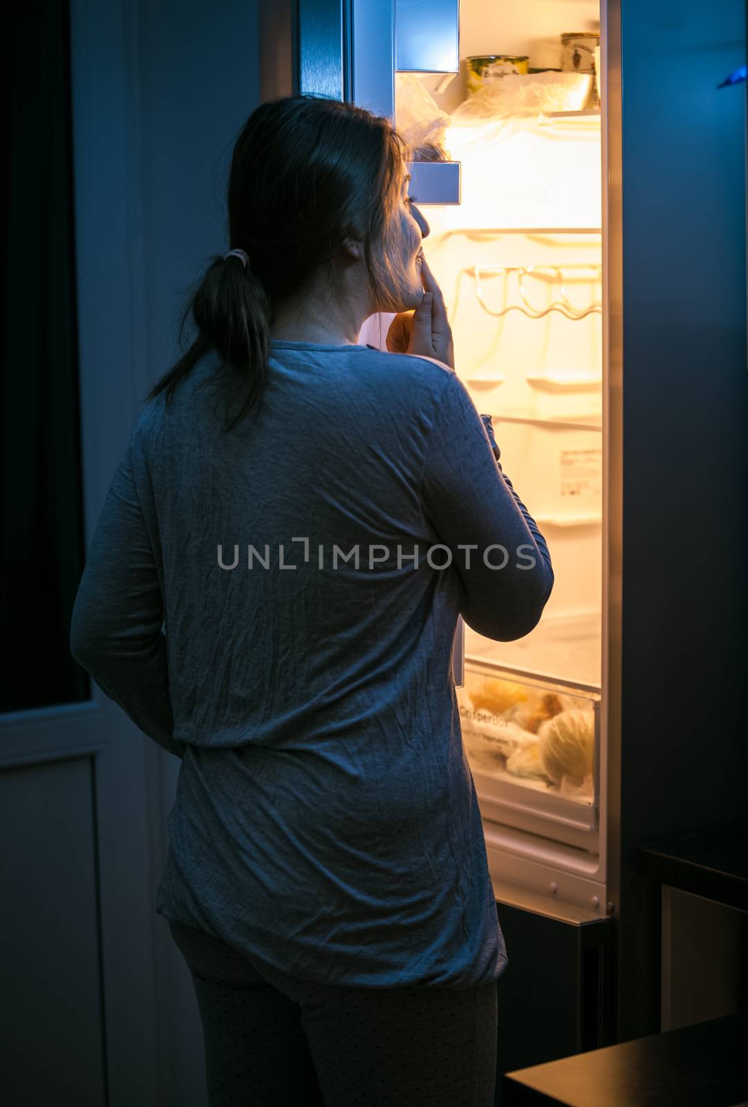 Photo of young woman looking inside the fridge at late night