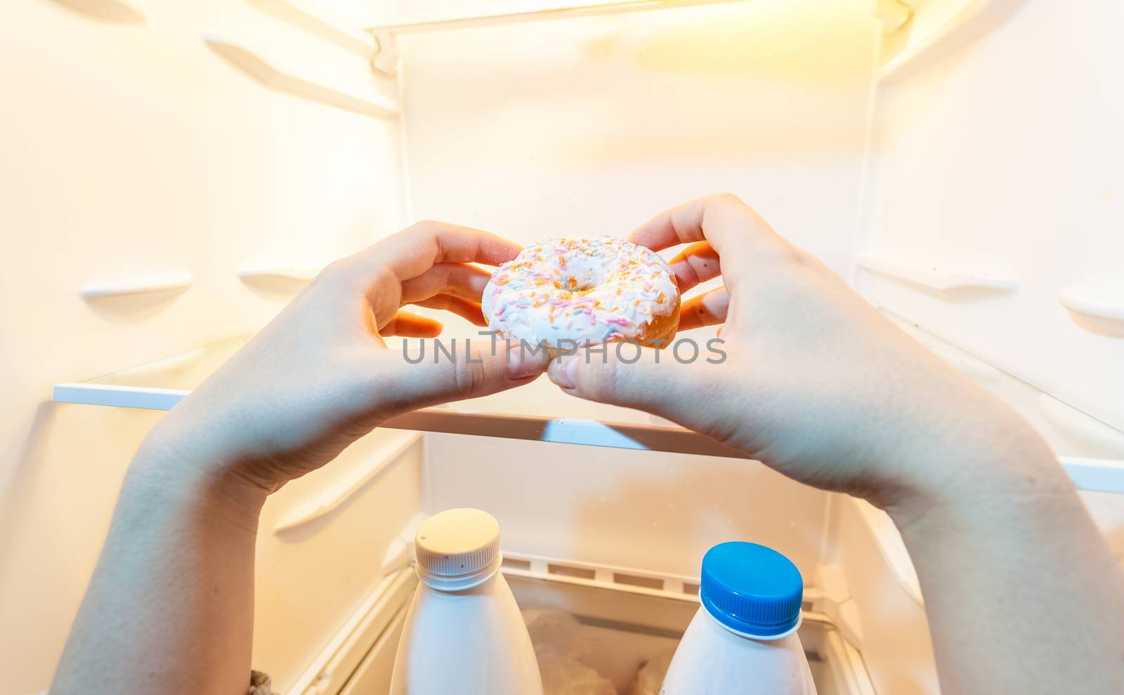 Closeup photo of female hand taking donut from refrigerator