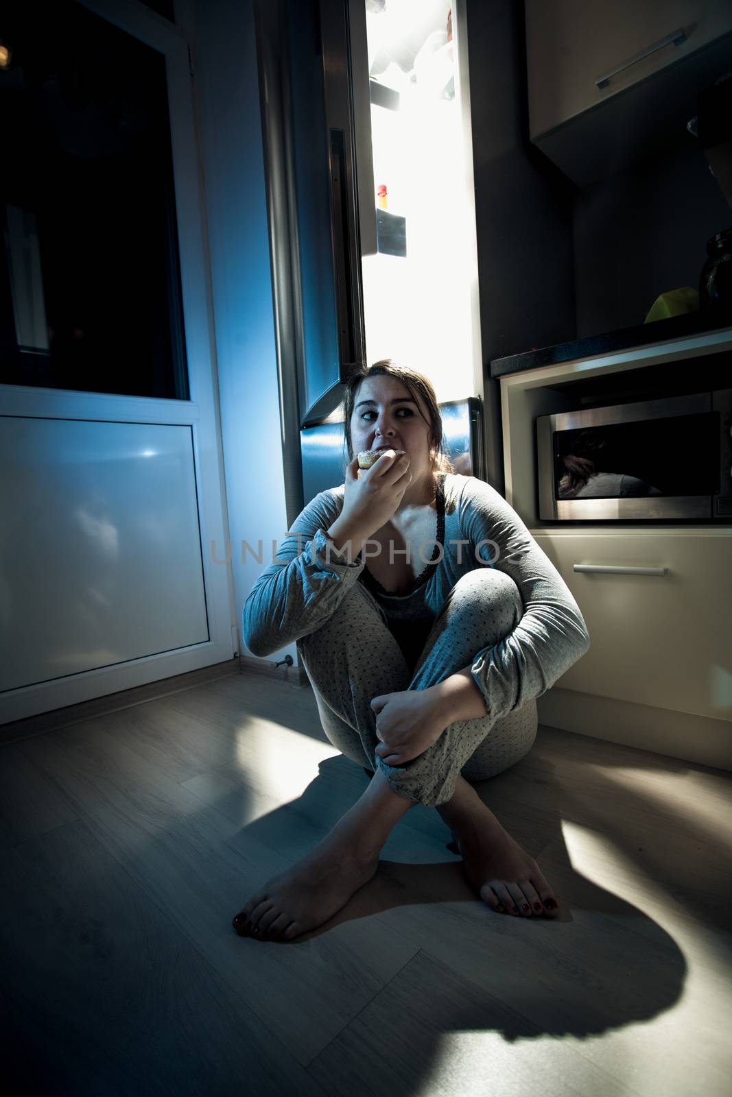 Woman eating donut on kitchen at night