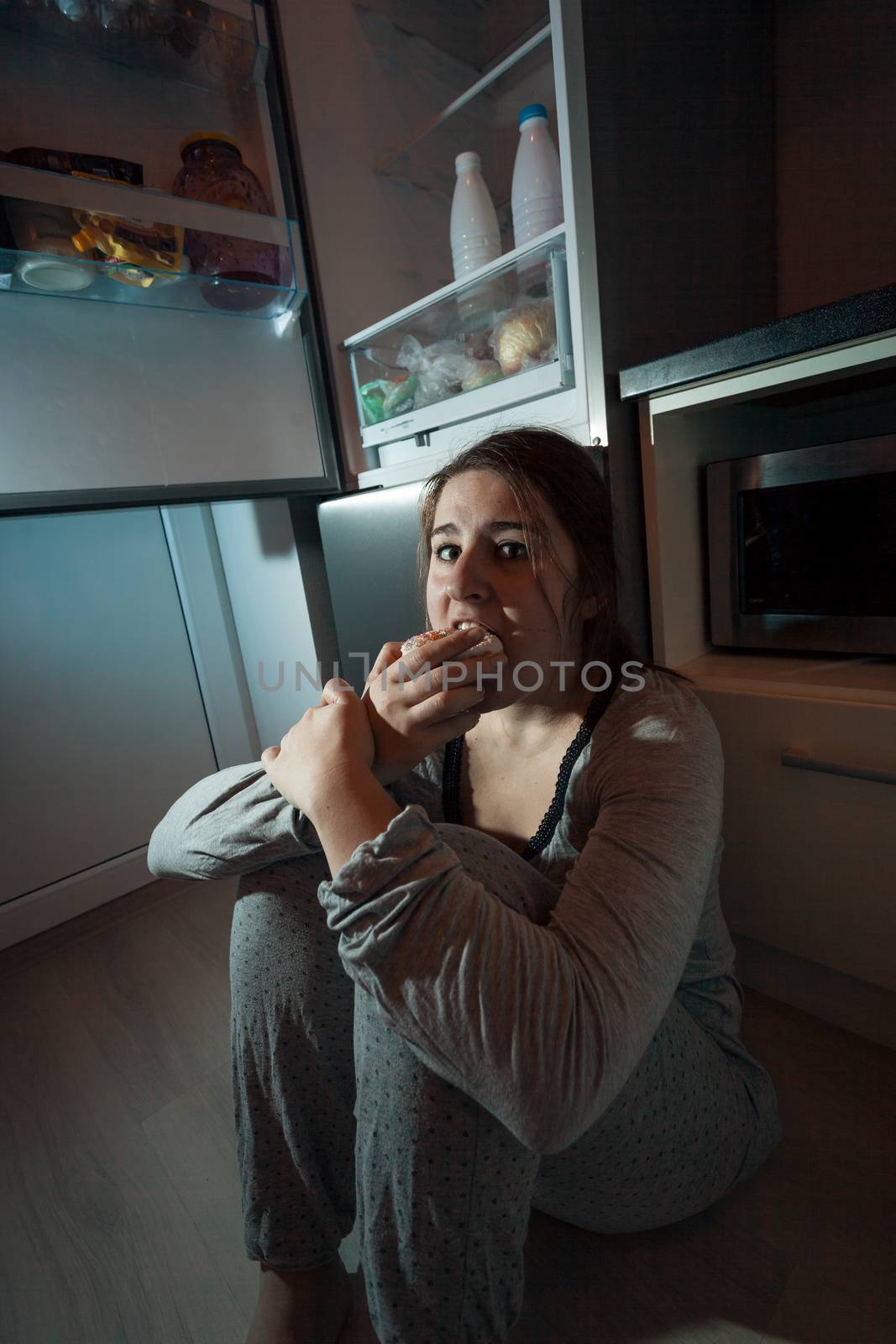 Hungry woman eating on floor at kitchen in night