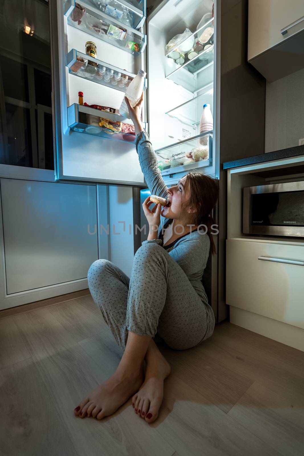 Woman eating on floor and reaching milk from fridge by Kryzhov