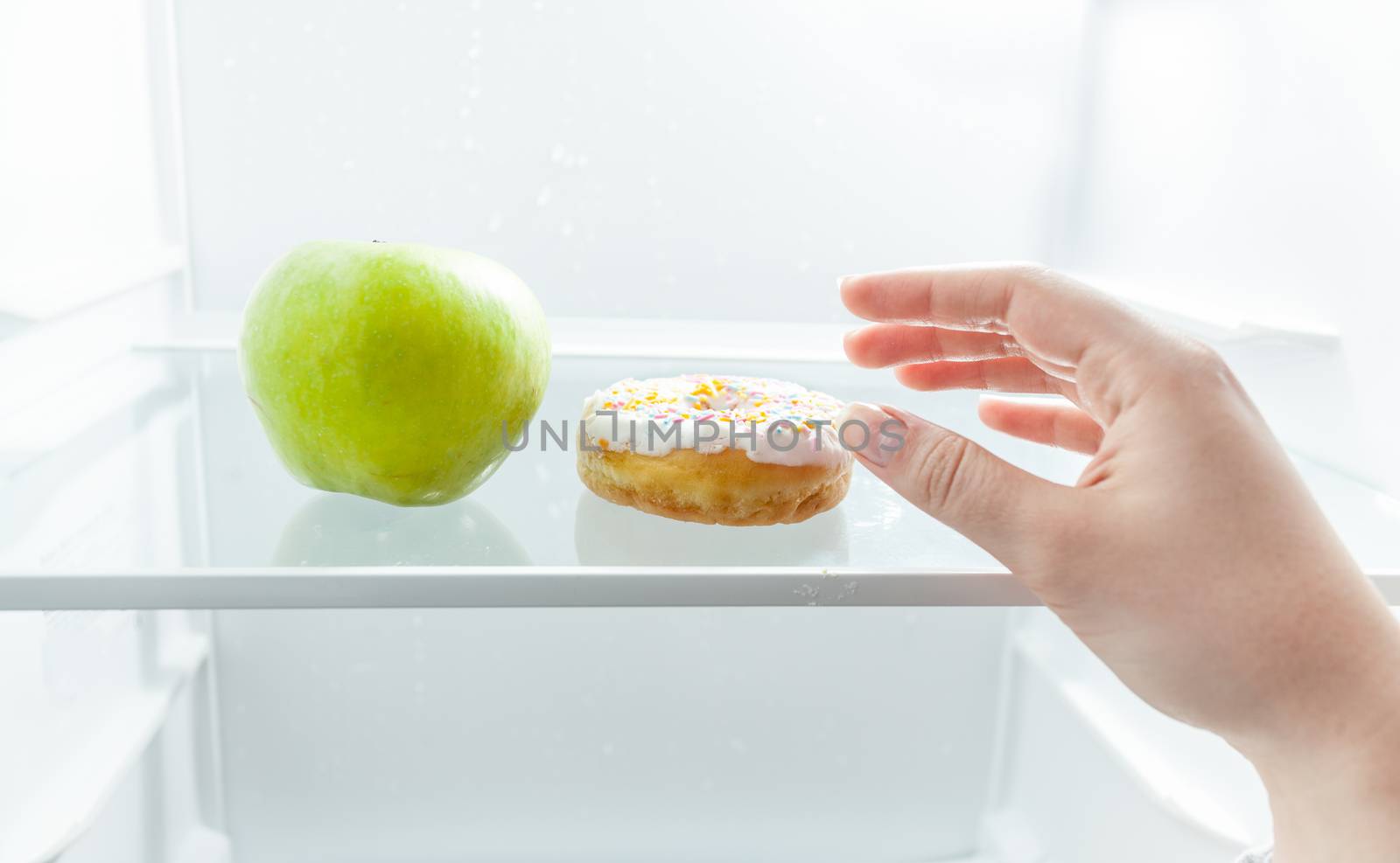 Closeup portrait of hand choosing between apple and donut at fridge
