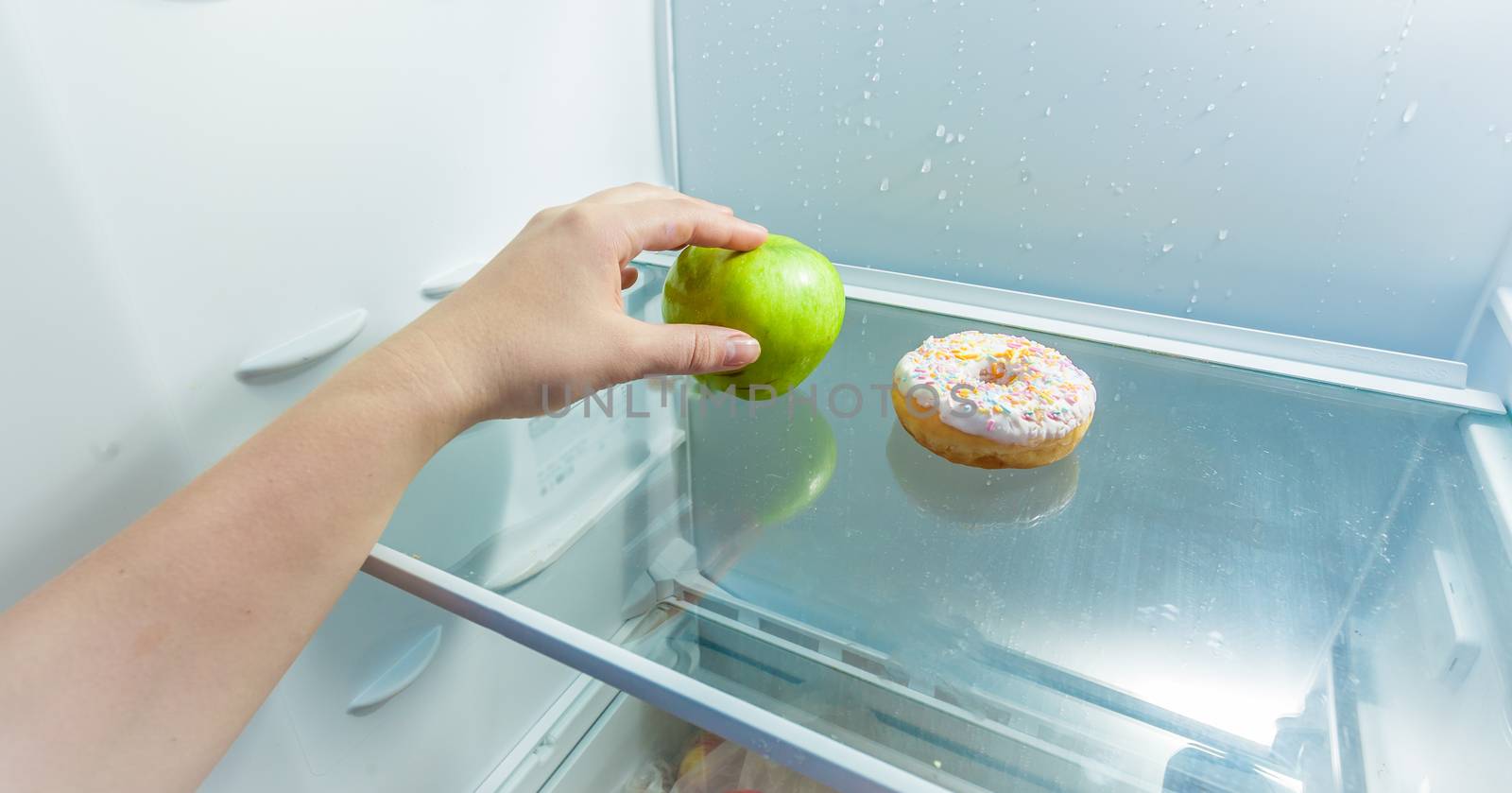 Photo of hand taking apple instead of donut lying in fridge
