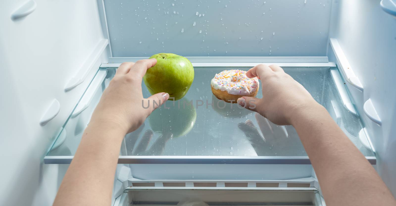 Closeup portrait of hands taking green apple and donut from fridge
